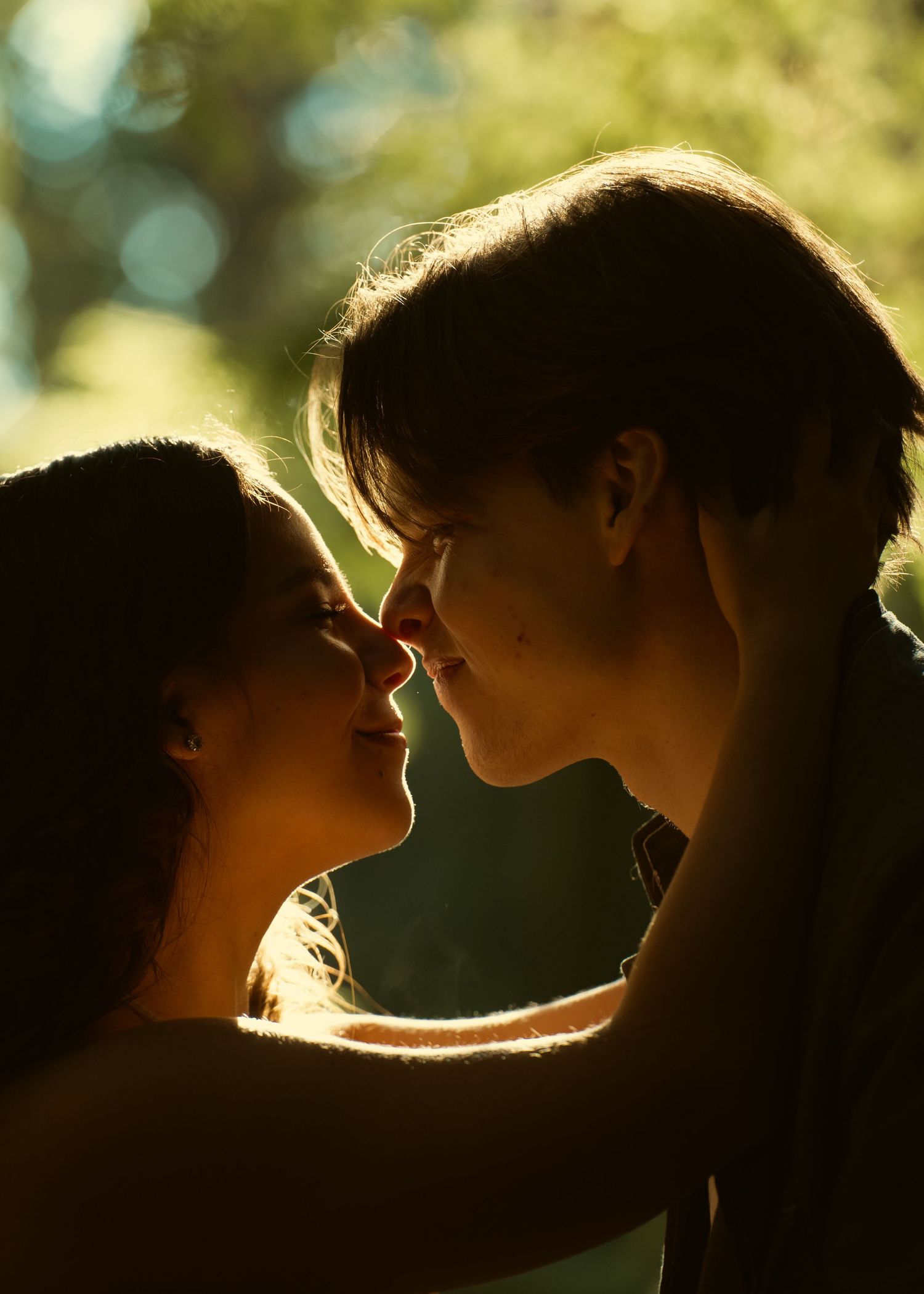 Romantic couple sharing an intimate moment in golden sunlight, faces close together in a tender almost-kiss outdoors.