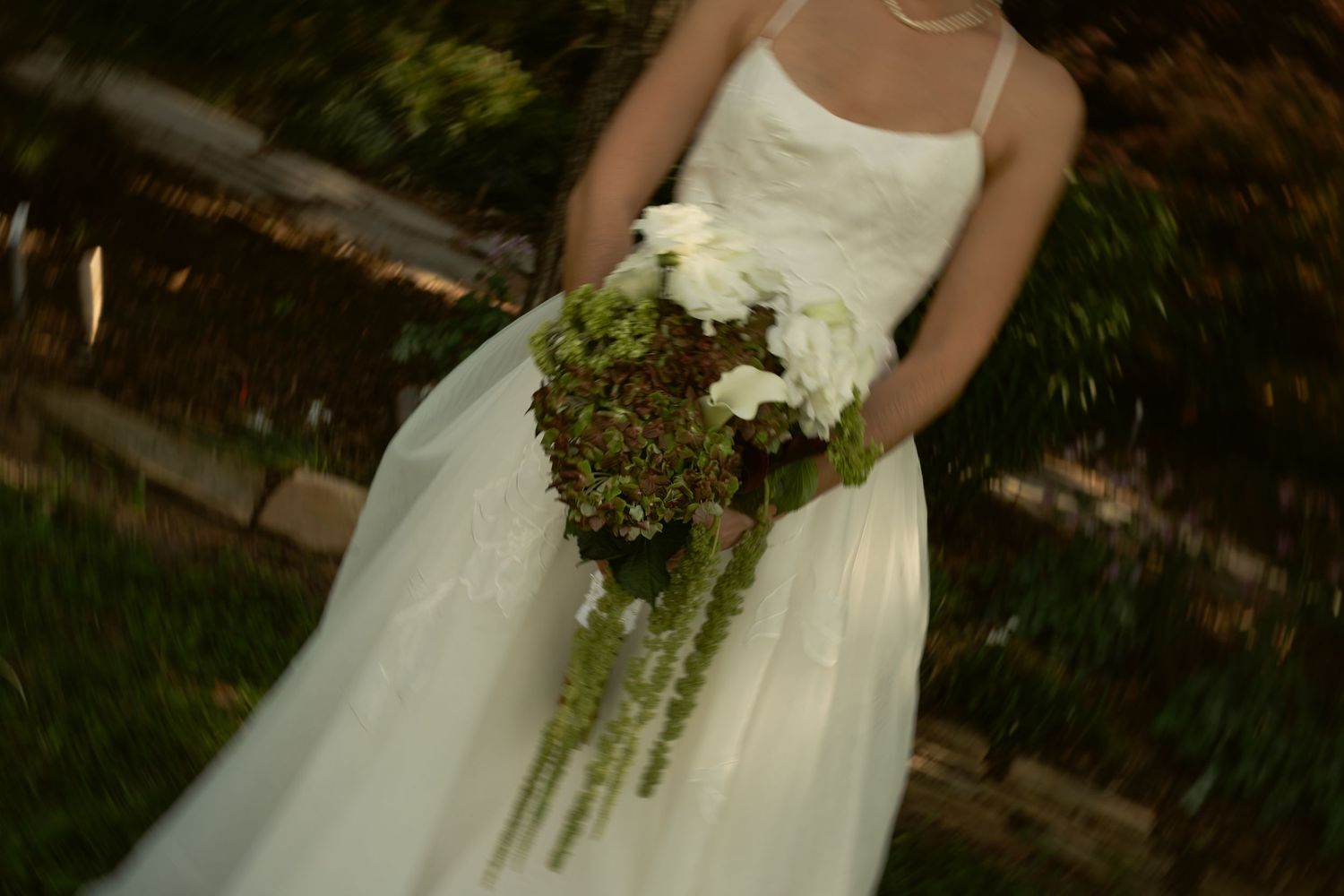 Bride in white gown holding green hydrangea and white floral bouquet outdoors.