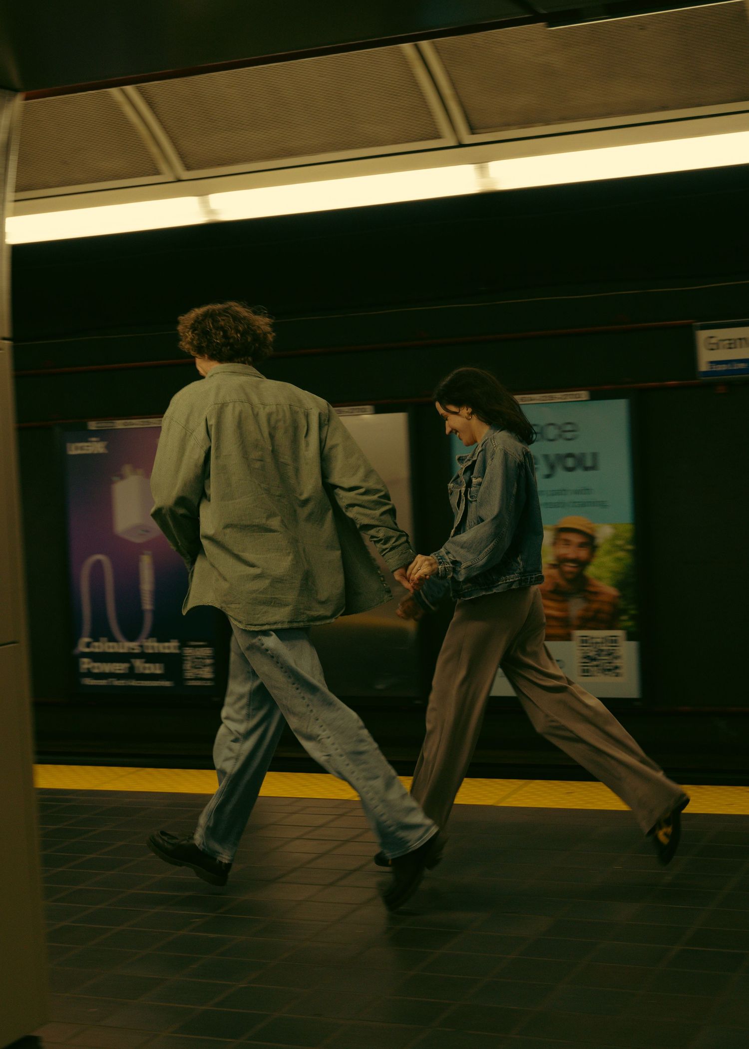 Two people running together in a subway station with dark lighting.