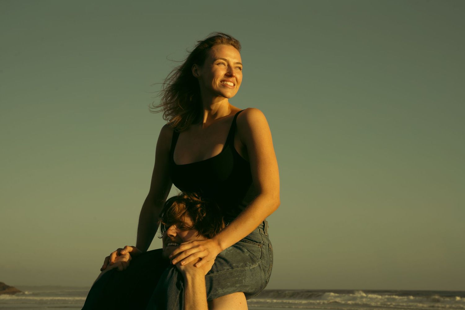 Person sitting on beach during golden hour with wind-swept hair.