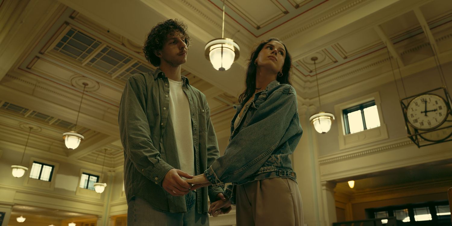 Two people interact in a grand hall with decorative ceiling and hanging lights.