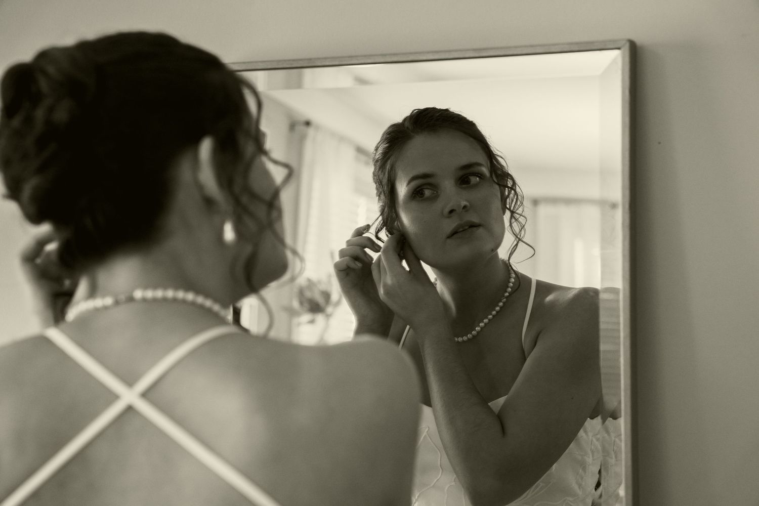 Black and white photo of bride adjusting earring while looking in mirror before wedding.