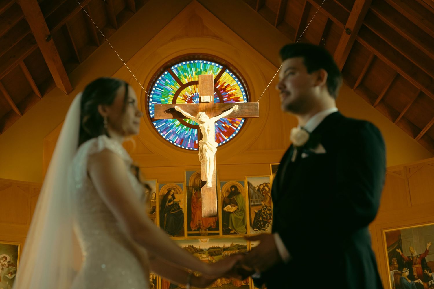 Wedding ceremony in church with stained glass window and crucifix in dramatic lighting.