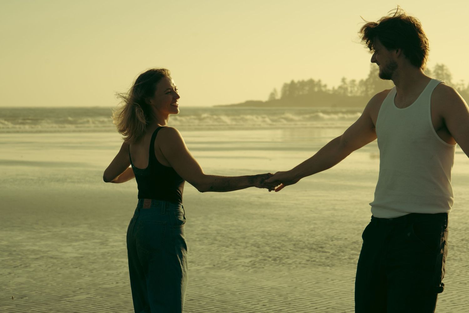 Two people holding hands while walking on beach at sunset.