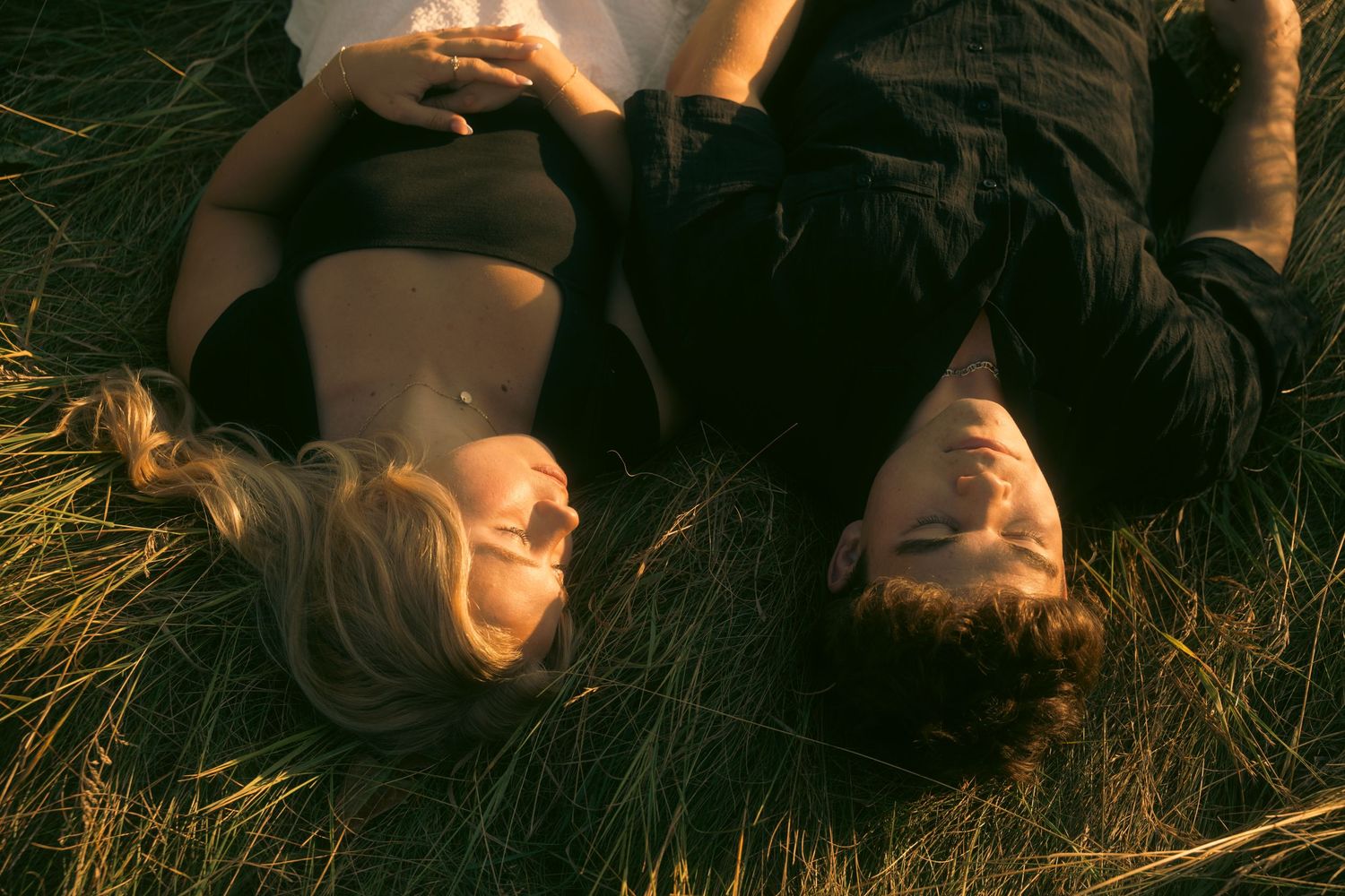 A couple lying in green grass together, gazing at each other in warm golden light.