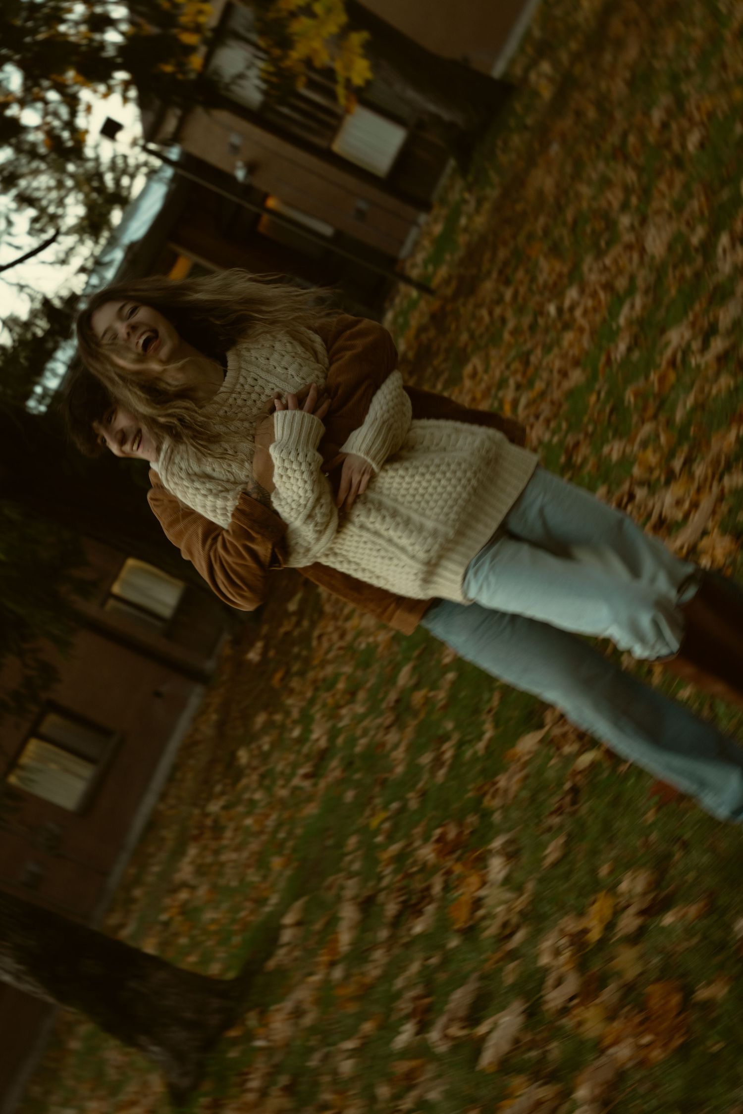 Person in a knit sweater and jeans standing among fallen autumn leaves.