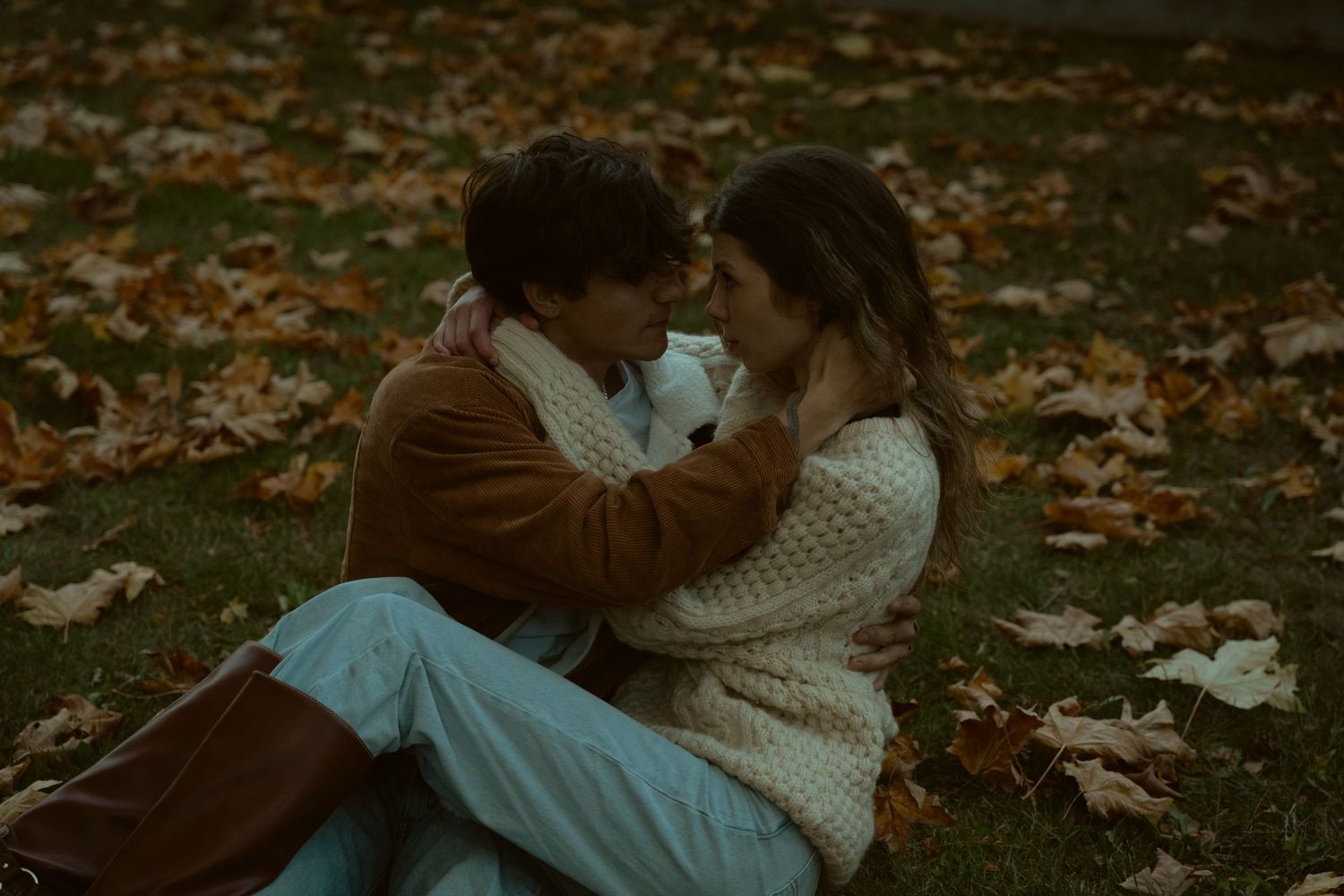 Couple resting on autumn ground surrounded by fallen leaves.