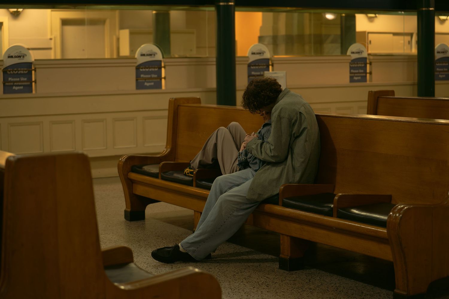 Two people sitting together on wooden church pews in warm lighting.