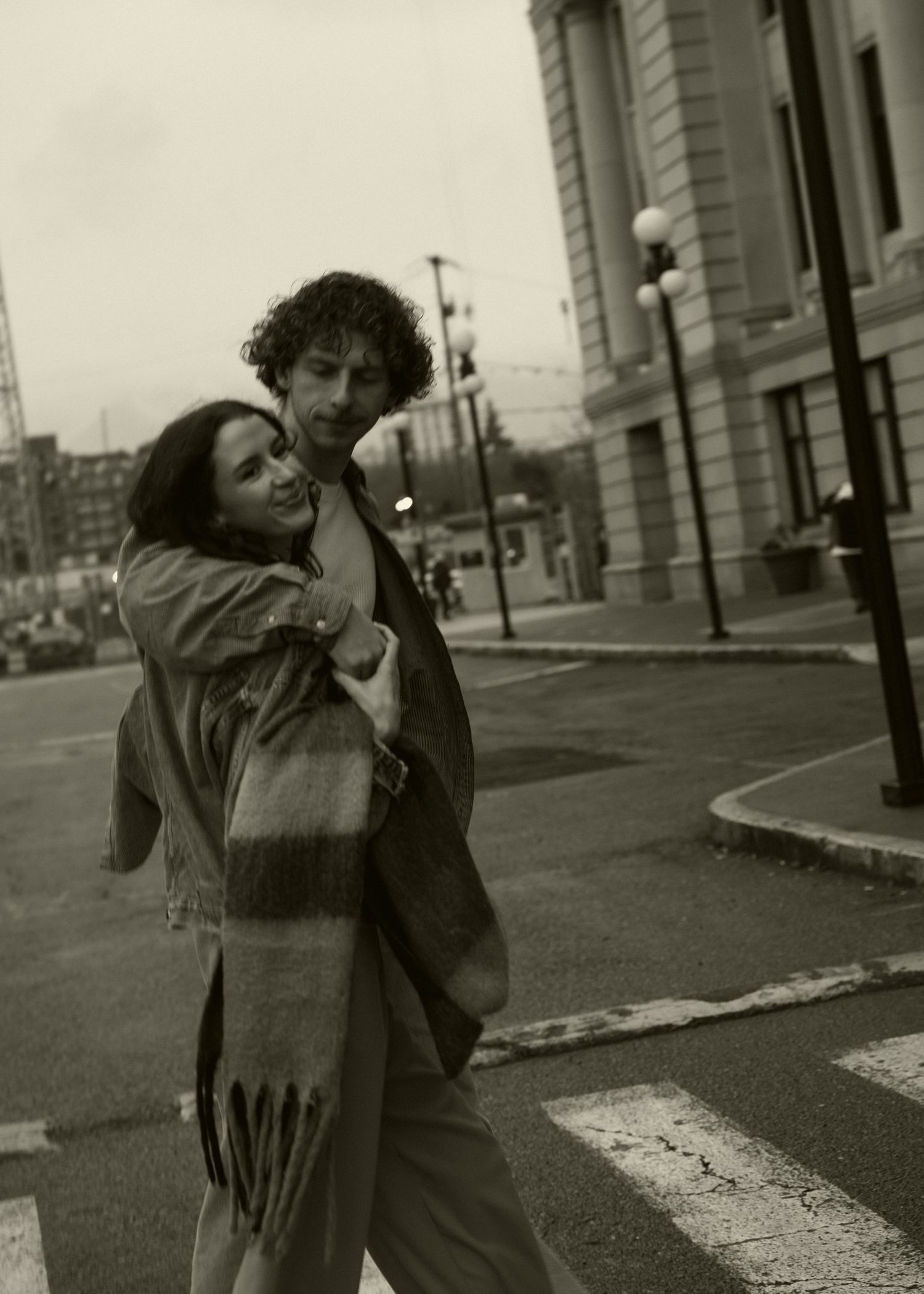 A couple embraces on a city sidewalk in black and white photography.