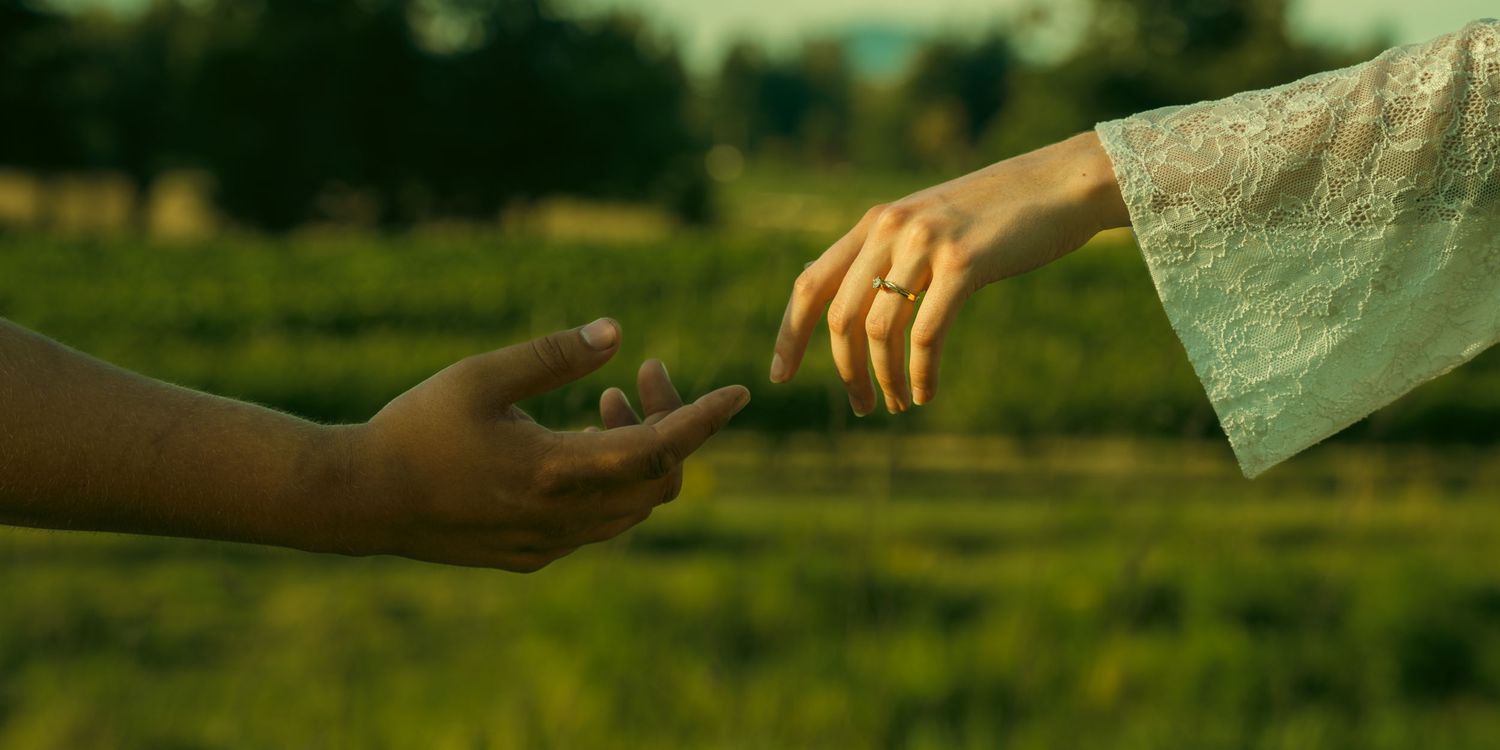 Hands reaching towards each other in a sunlit outdoor setting.