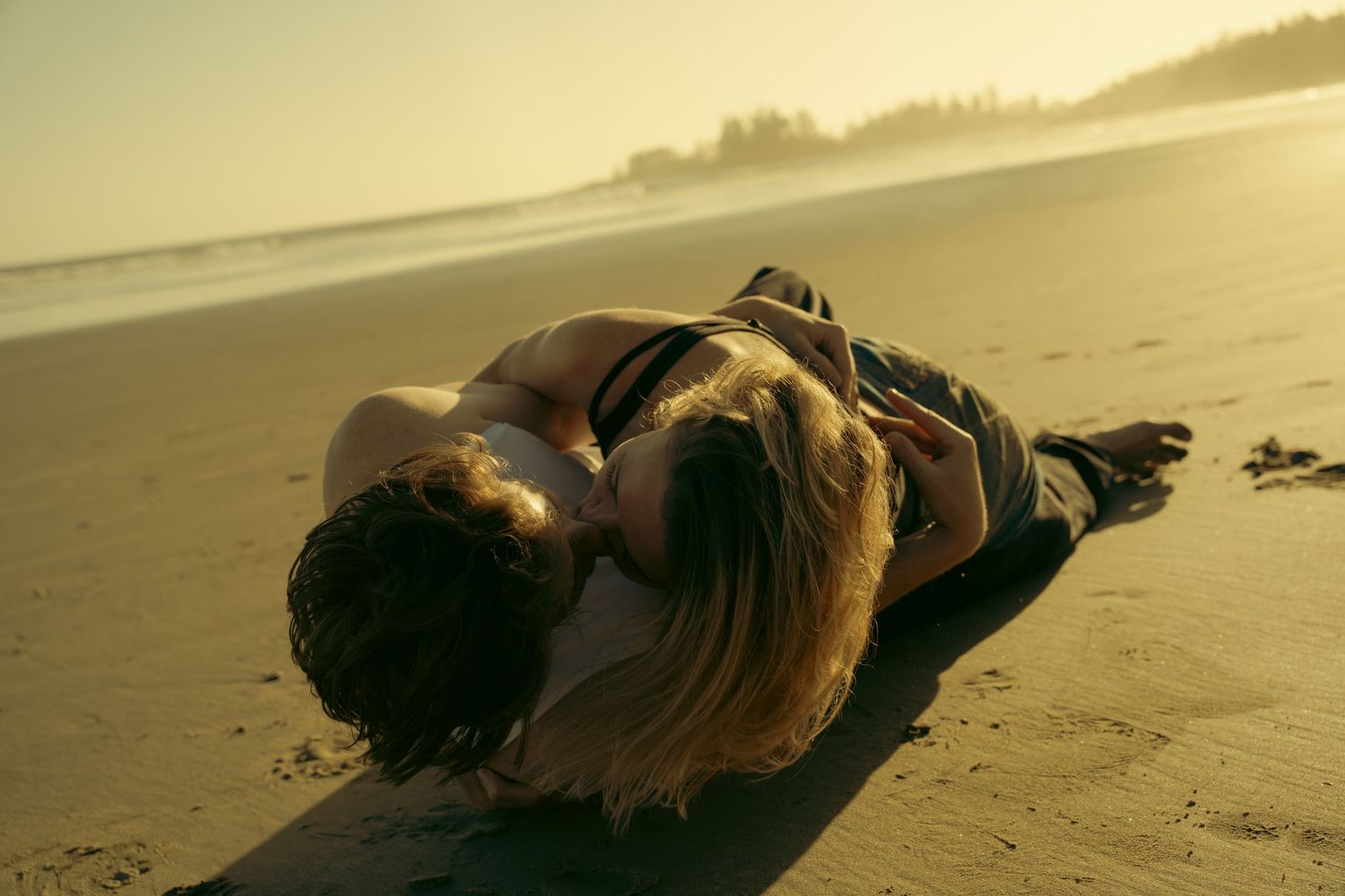 Two people embracing on sandy beach during golden hour.