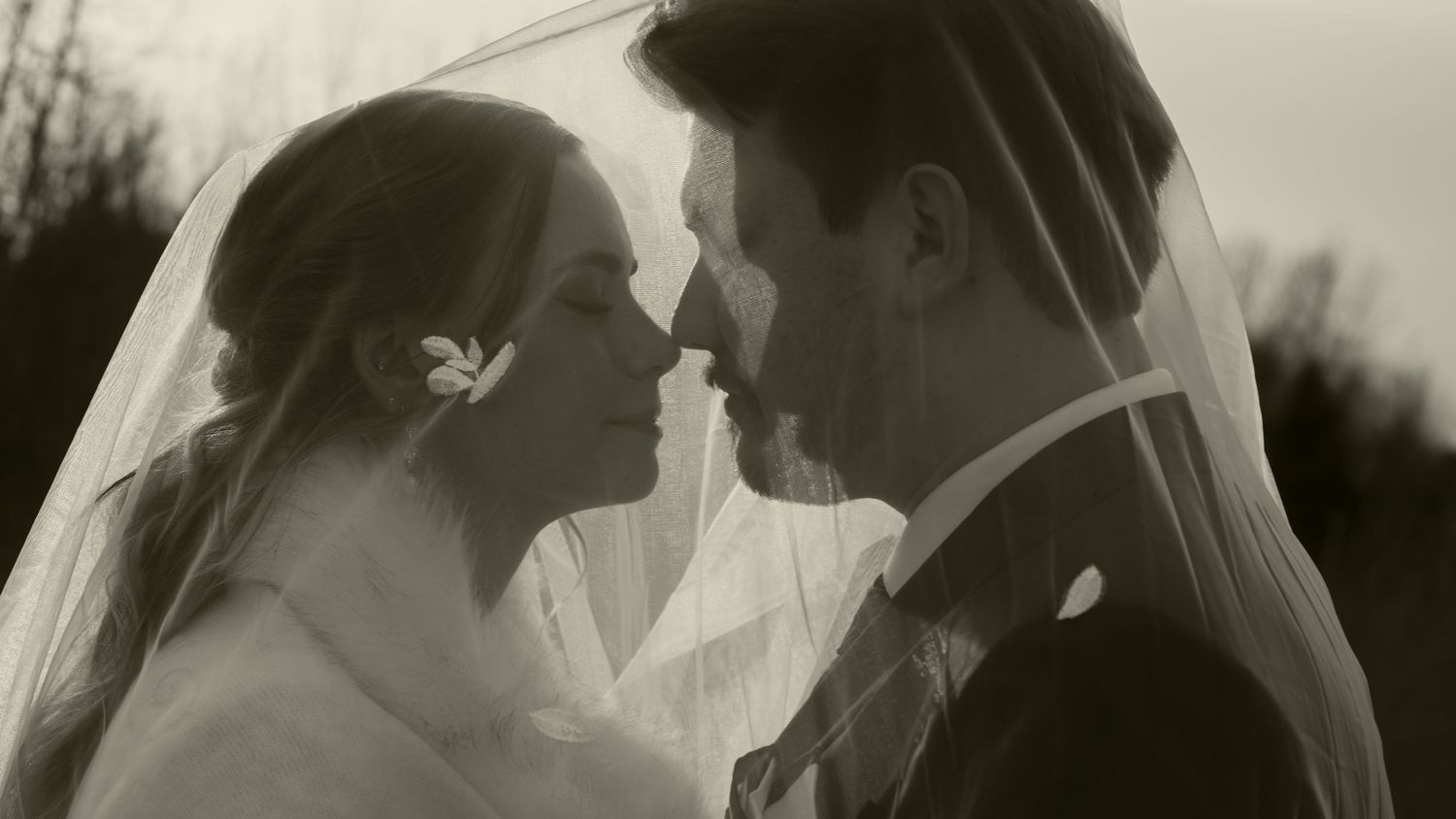 Intimate black and white portrait of newlyweds sharing a moment under a flowing veil.