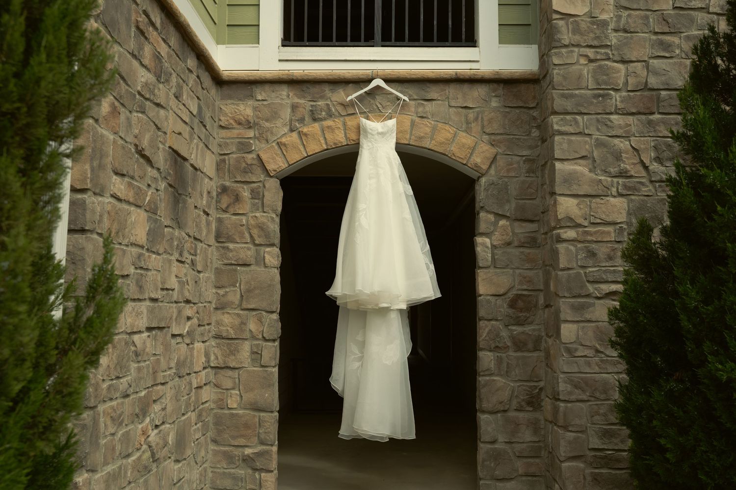 Elegant white wedding dress with veil hanging in a stone archway doorway before the ceremony.