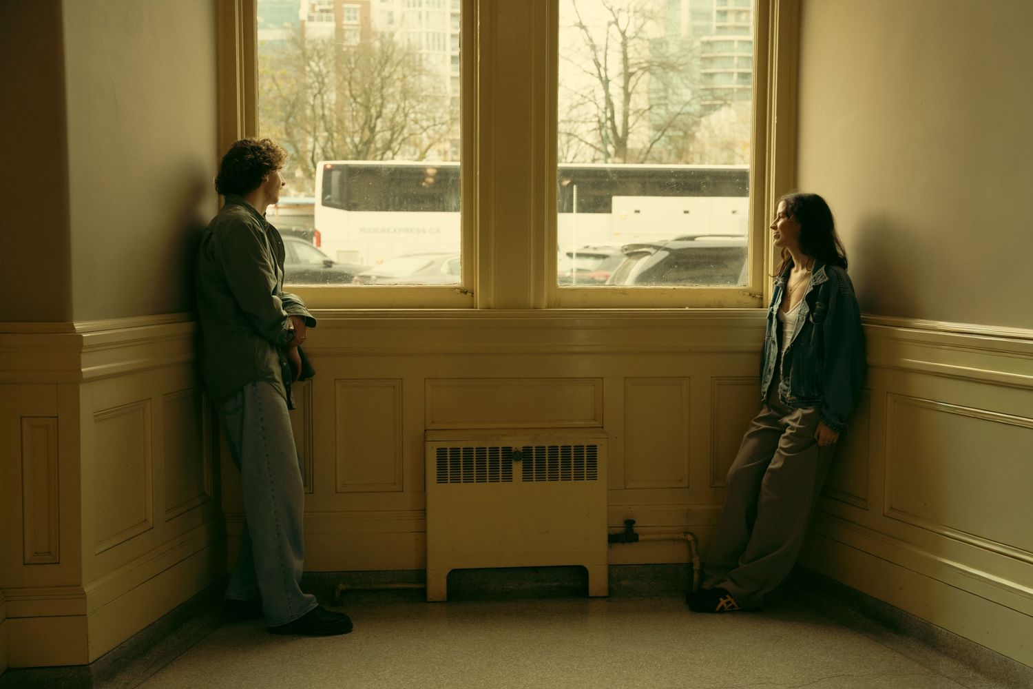 Sunlight streams through windows in a hallway where two people stand together.