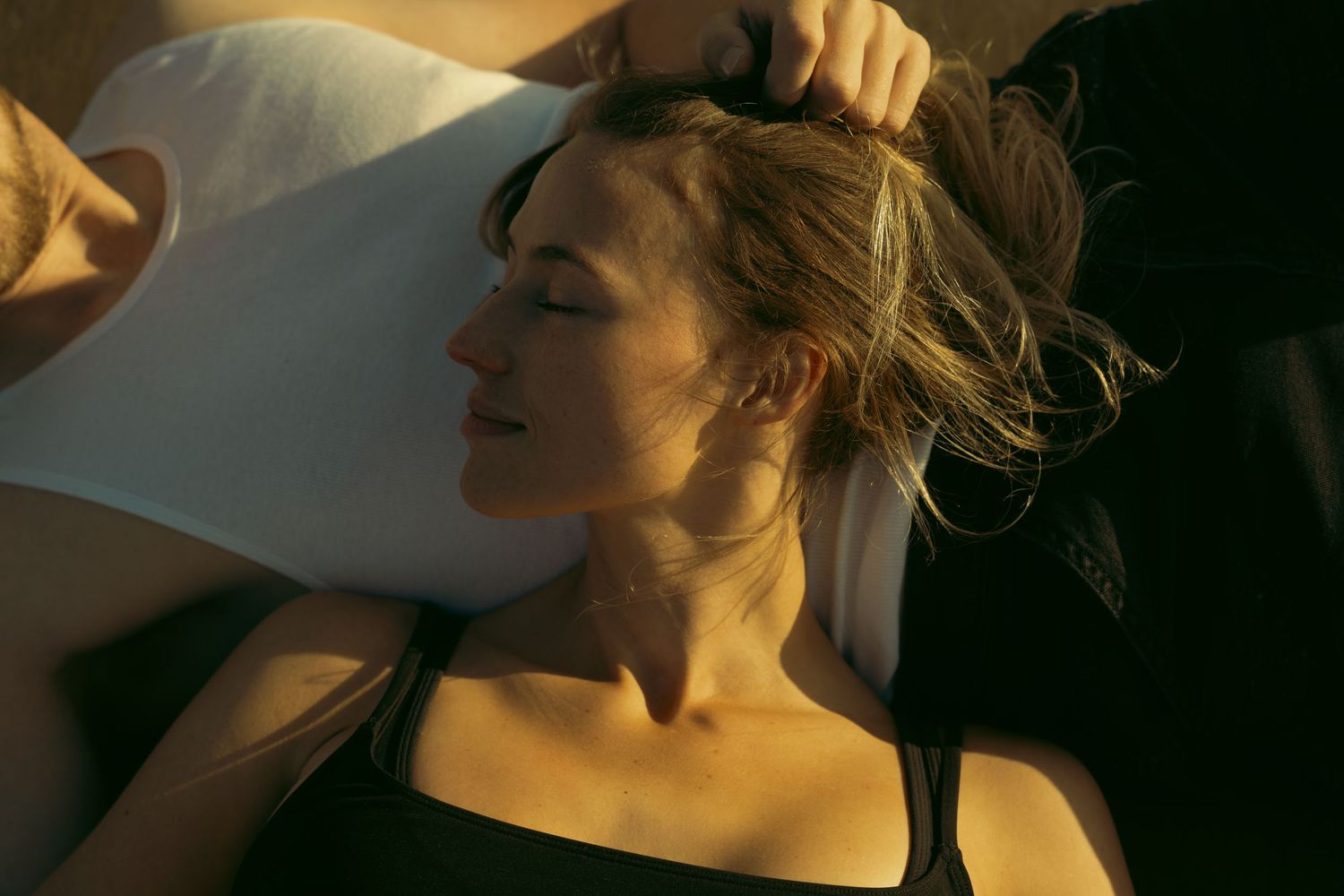 Person lying down with eyes closed in dramatic sunlit portrait.