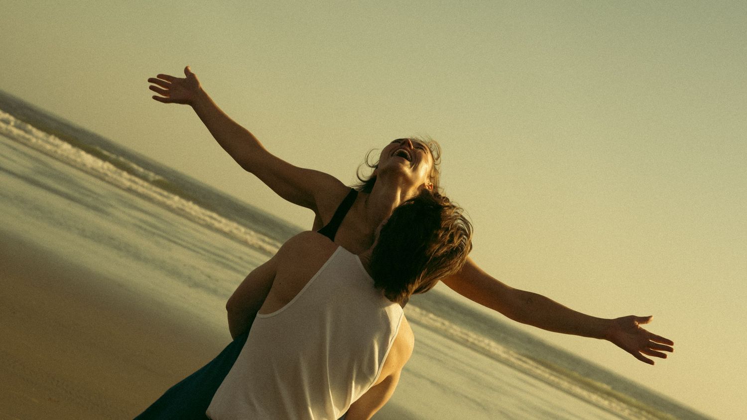 People enjoying freedom with outstretched arms on a beach at sunset creating silhouettes against the sky.