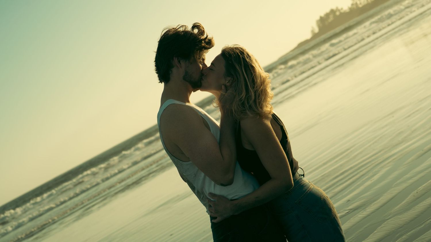 Couple in romantic embrace by waterfront during golden hour.