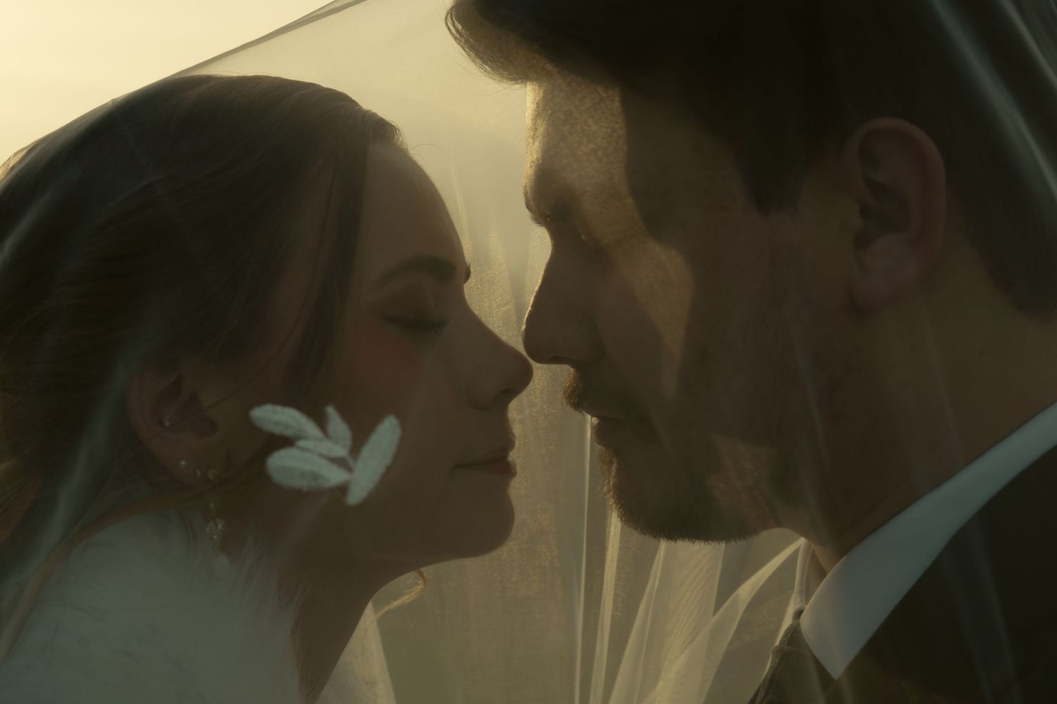 A couple shares an intimate moment during a wedding photoshoot with soft golden lighting.