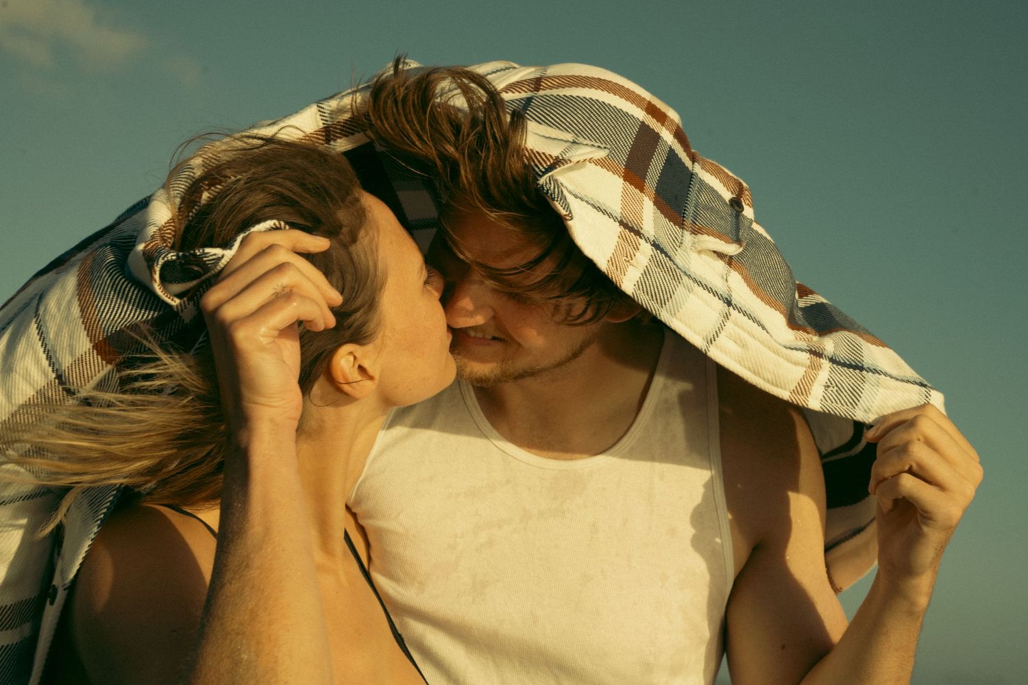 Couple sharing intimate moment under blanket in warm sunlight.