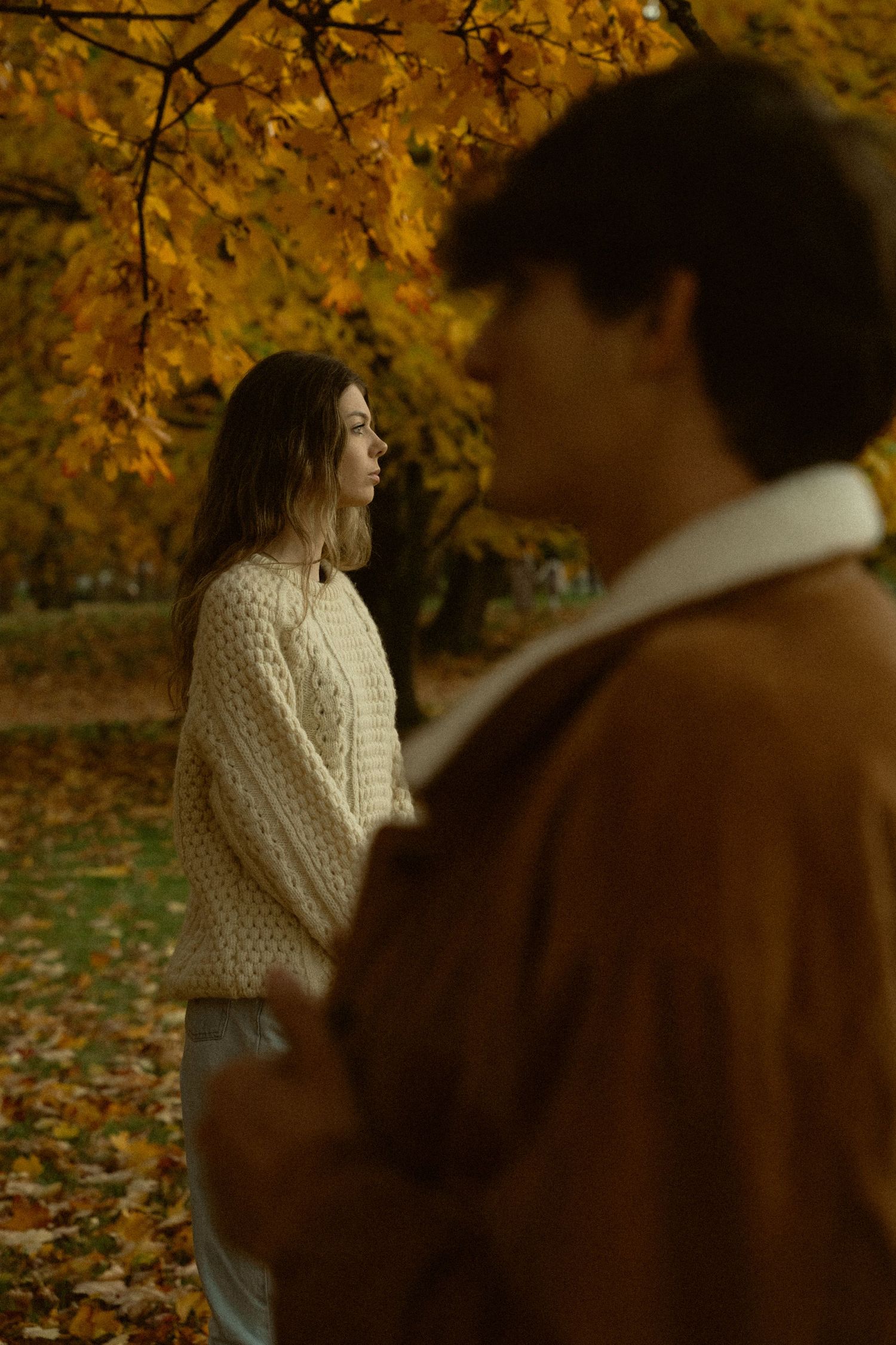 Couple in warm sweaters standing among fall foliage.