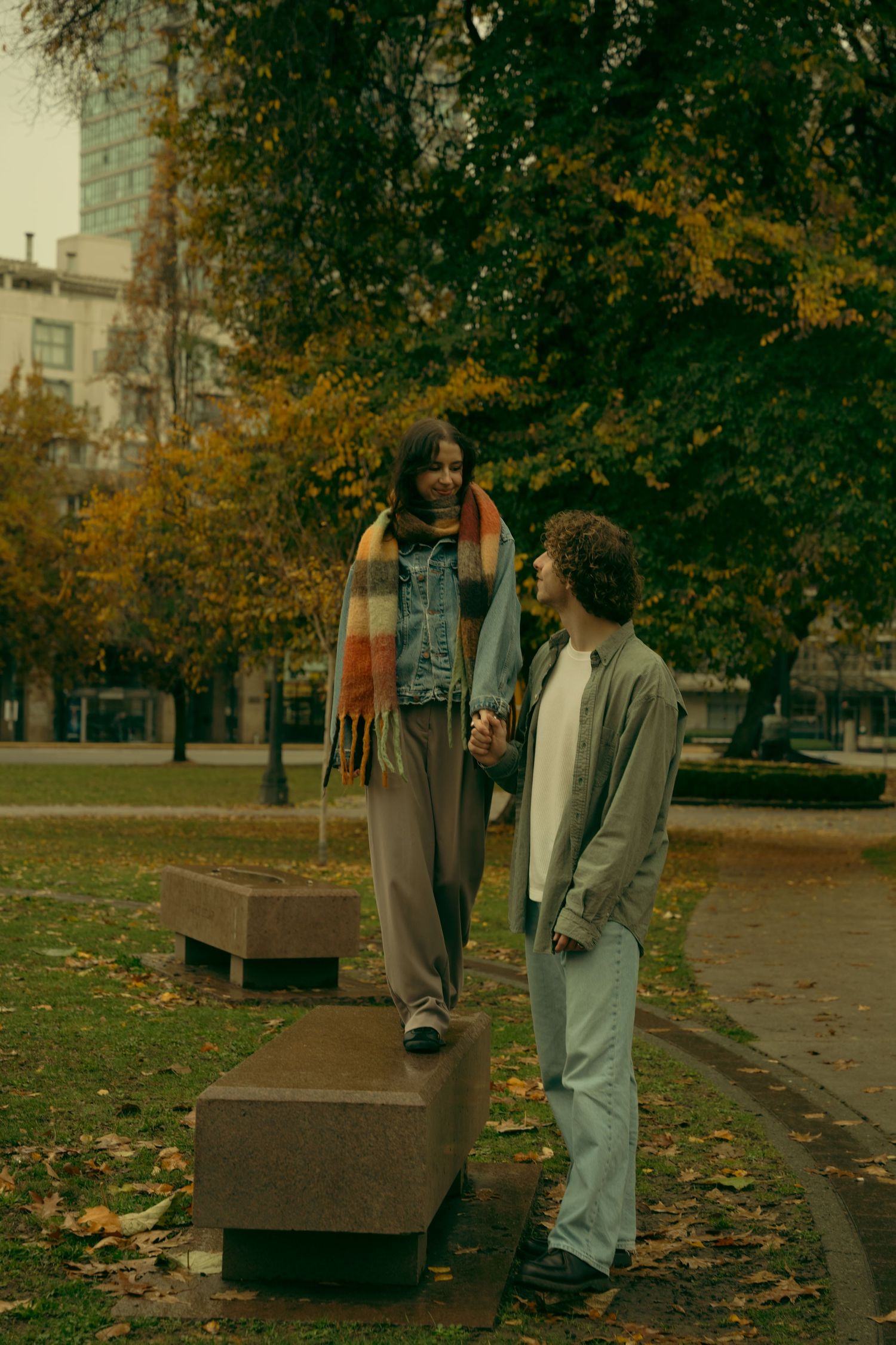 People strolling through a park with benches and autumn foliage in the background.