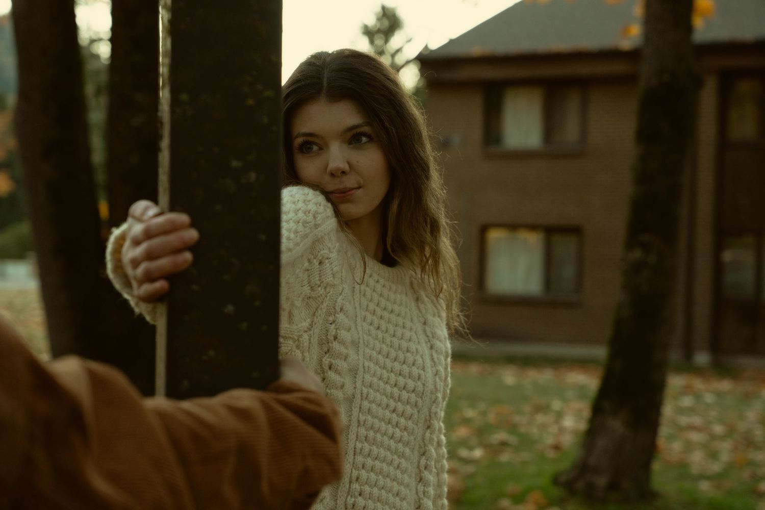 Person in white knit sweater standing among autumn trees at golden hour.