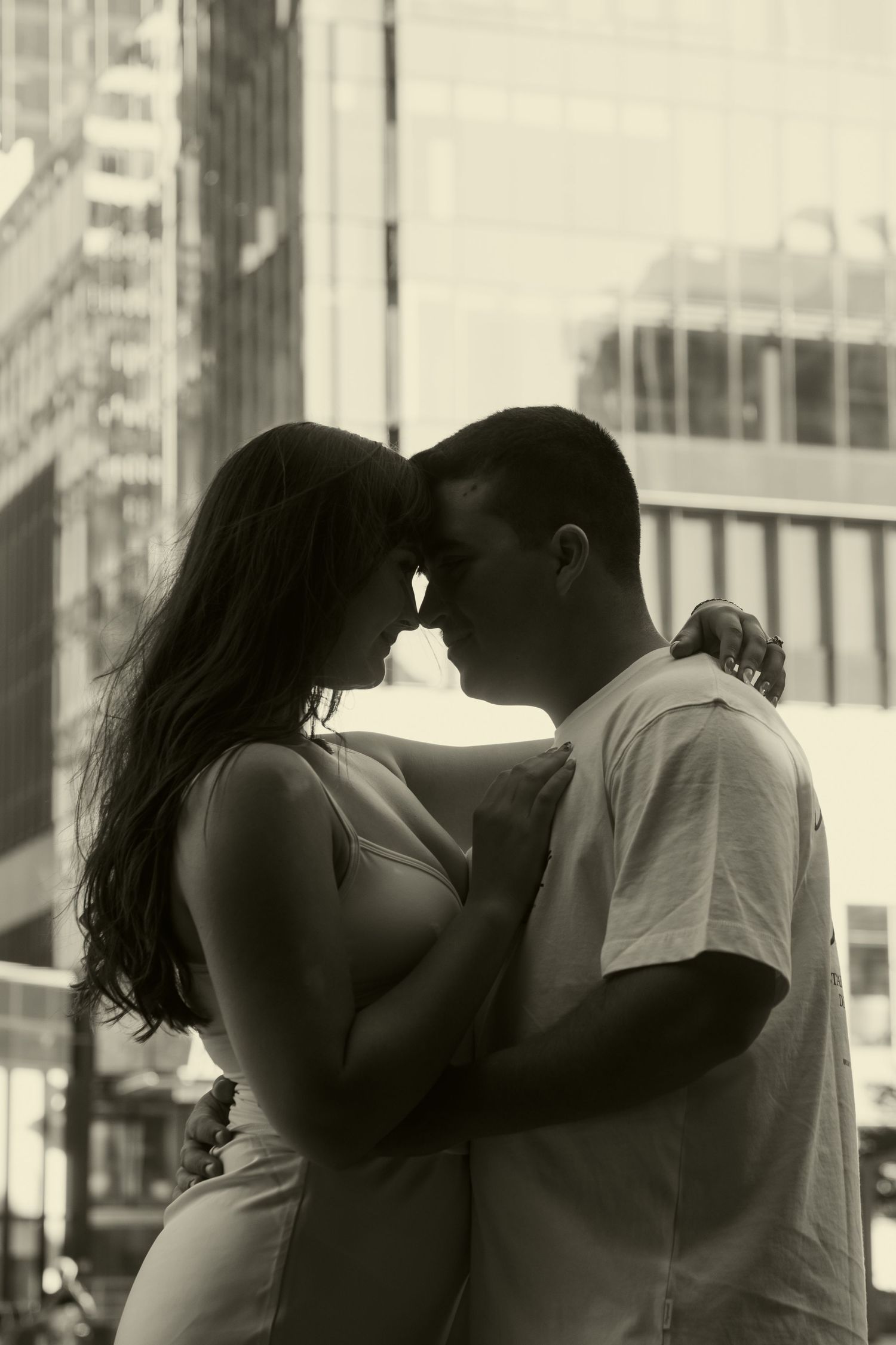 Black and white photo of a romantic couple embracing in an urban cityscape with skyscrapers in the background.