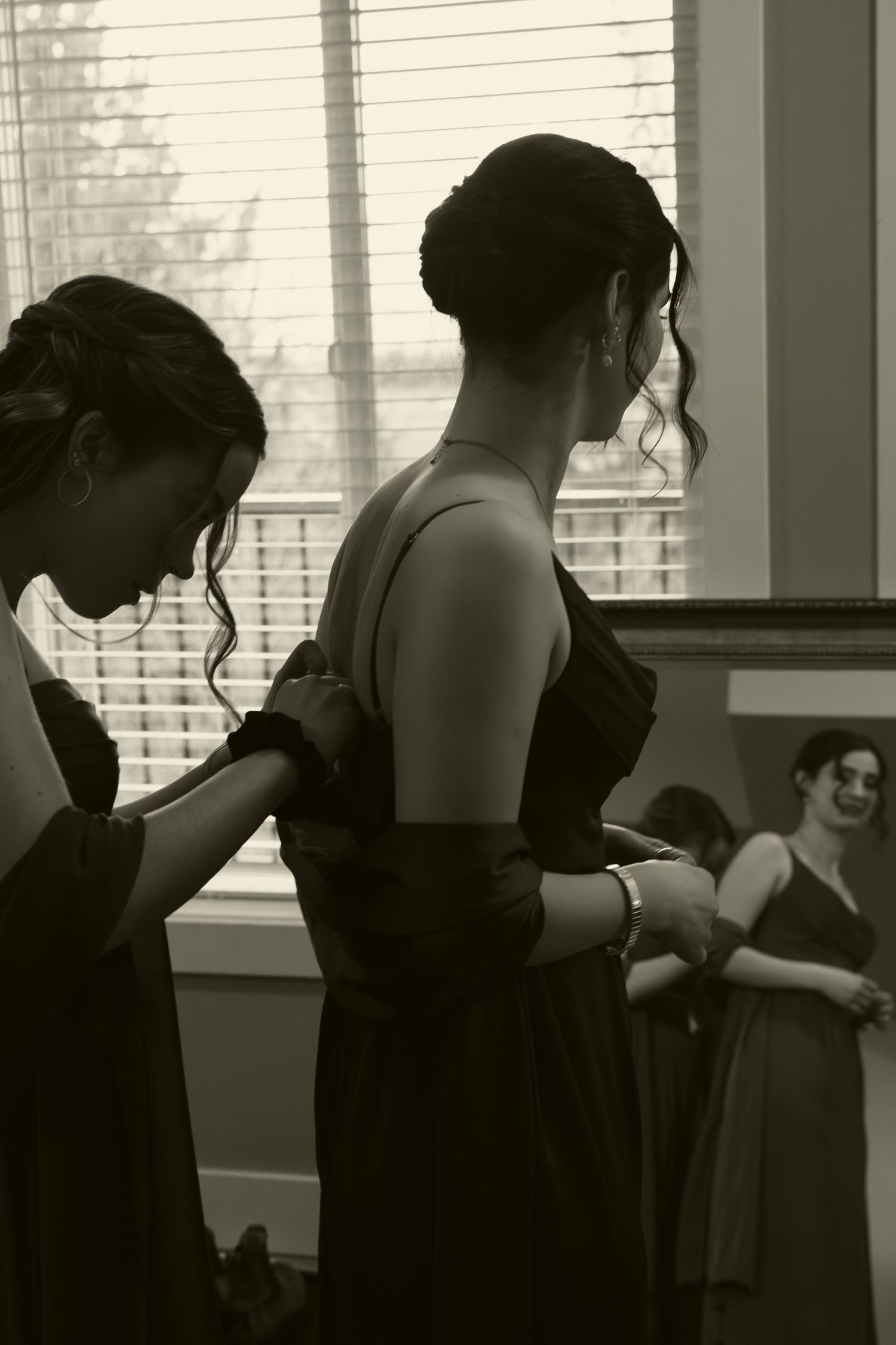 Two people adjusting formal attire by a window in black and white photography.