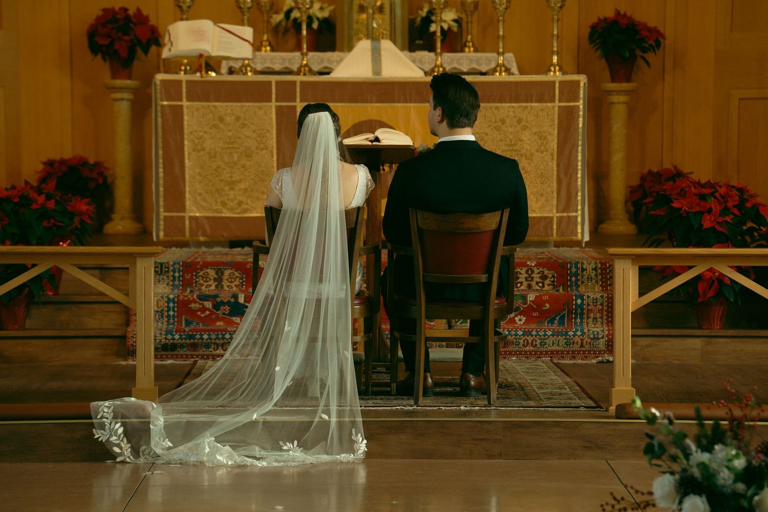 A couple seated at the altar during their wedding ceremony with floral decorations and candles.