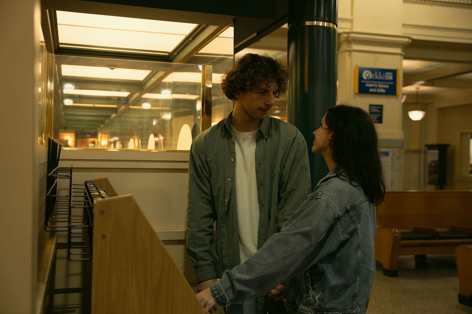 Two people stand in a brightly lit institutional hallway with white walls.