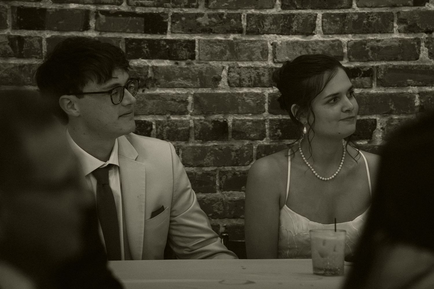 Bride and groom share a quiet moment seated together at wedding reception in black and white.