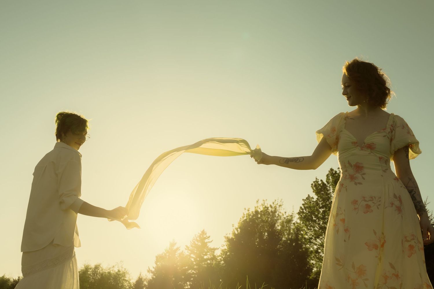 Couple sharing a yellow scarf at golden sunset outdoors.