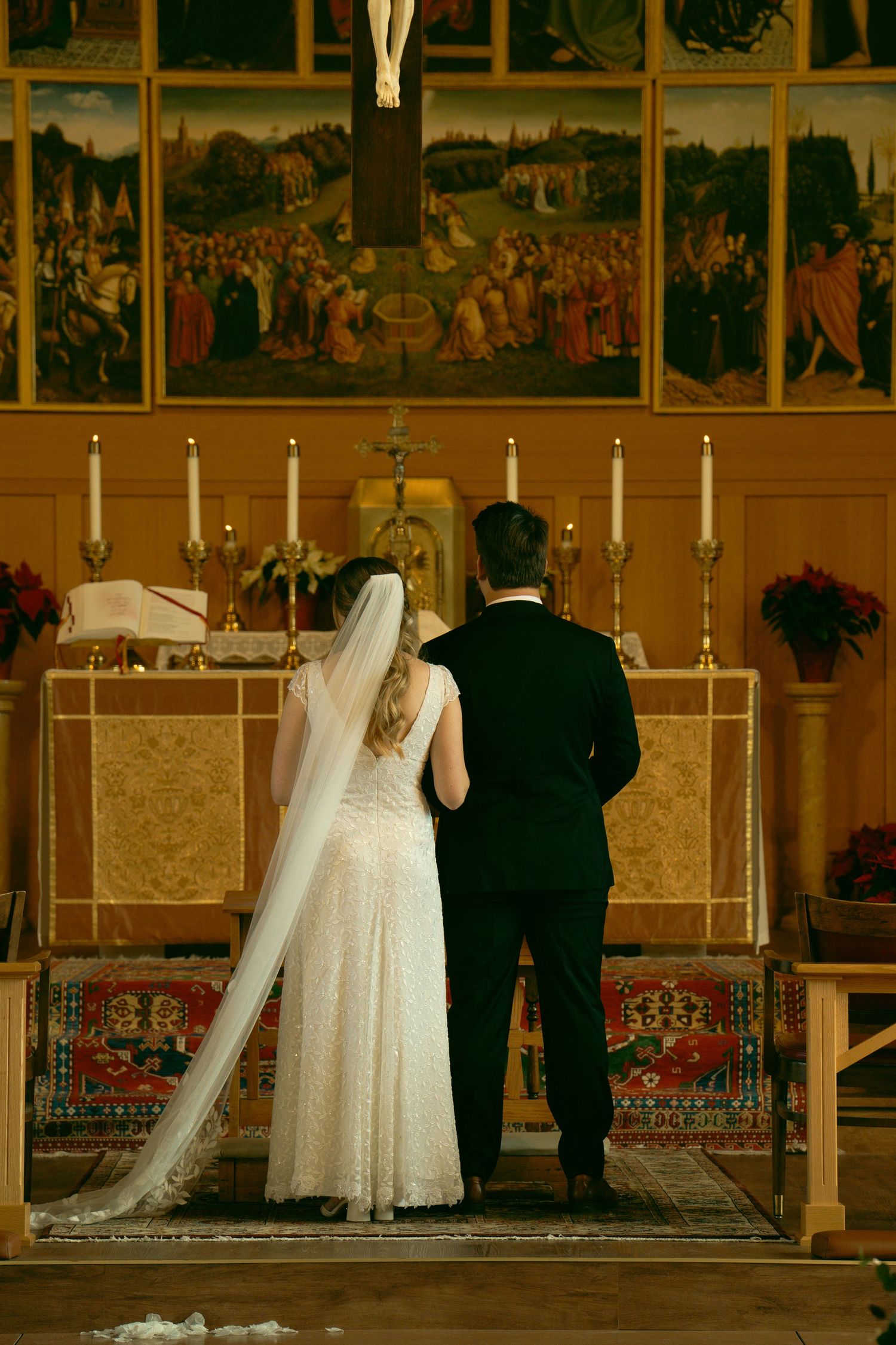A couple stands at the church altar beneath religious artwork and candlelight during their ceremony.