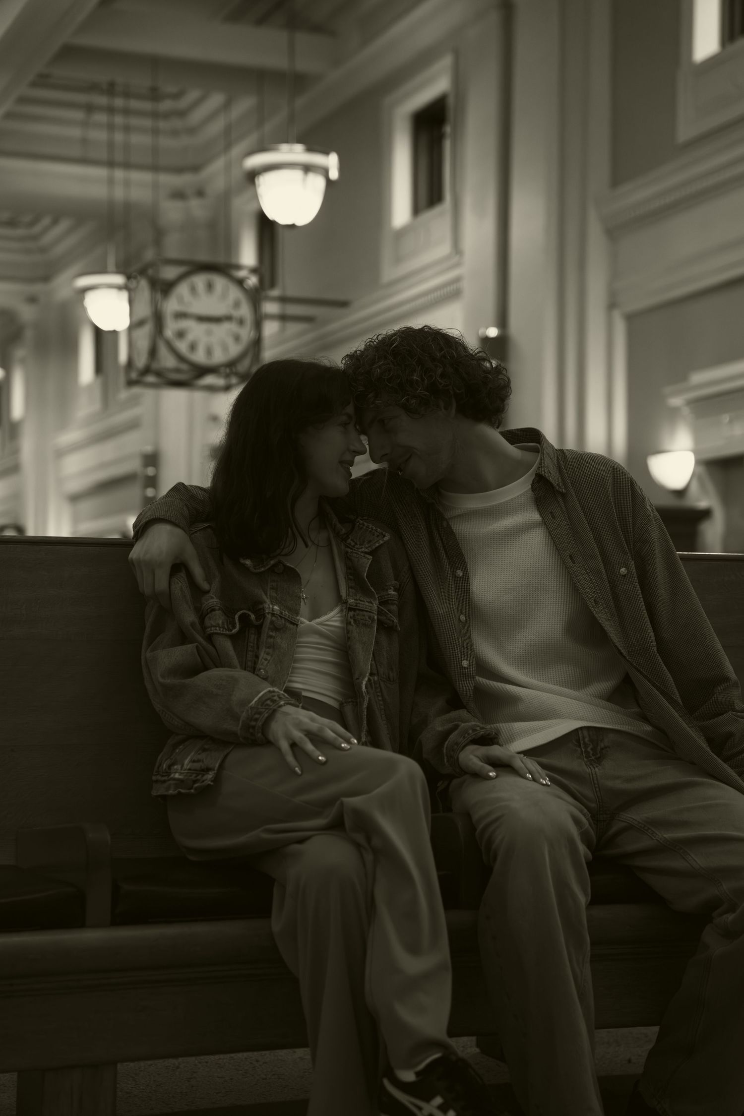 Two silhouettes lean close together on a bench in a building with classic architecture.