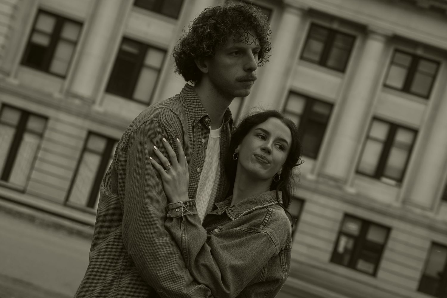 Two people share an intimate moment against an urban backdrop in sepia tones.