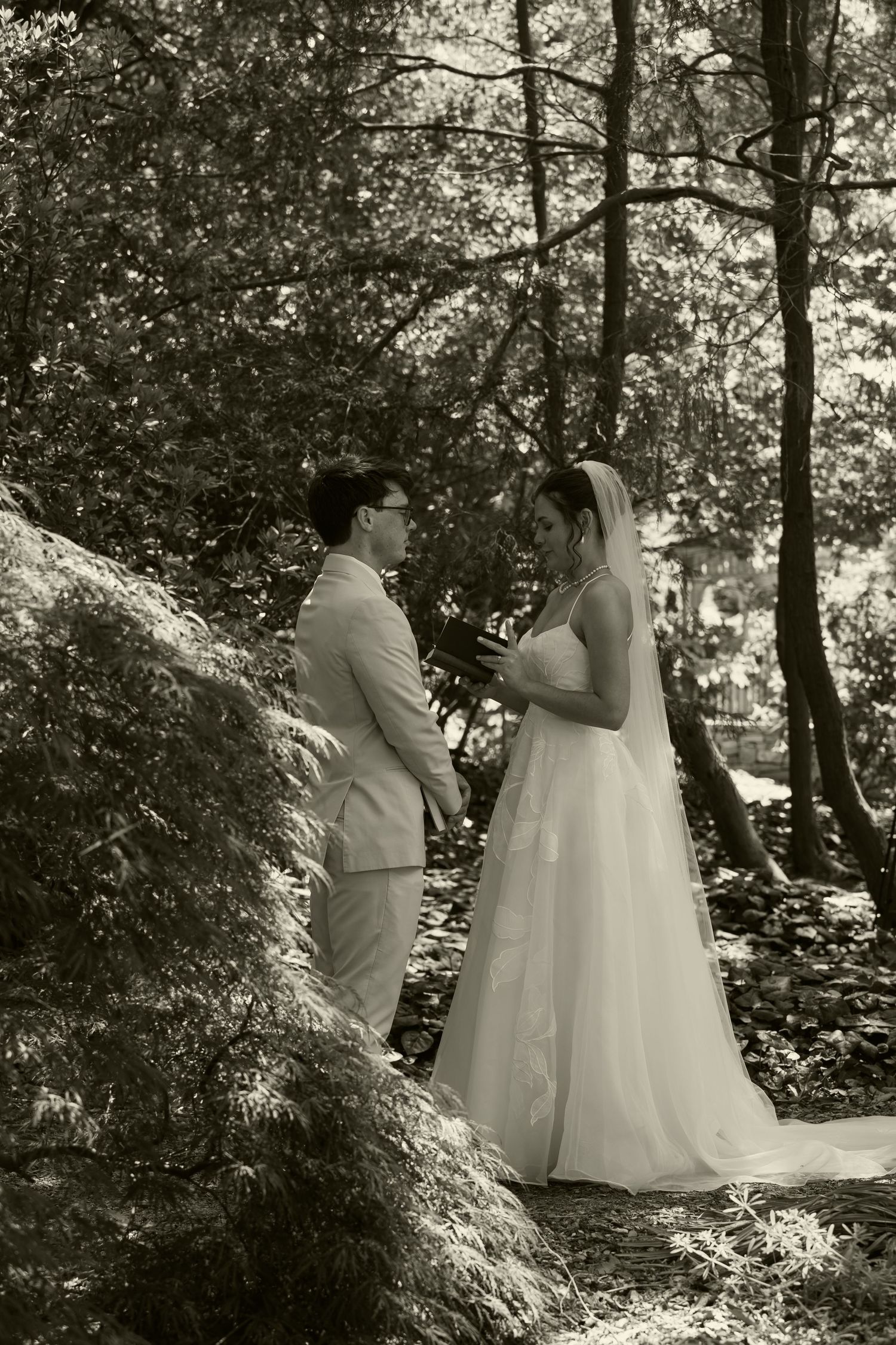 Black and white photo of bride and groom sharing intimate moment among lush garden trees.