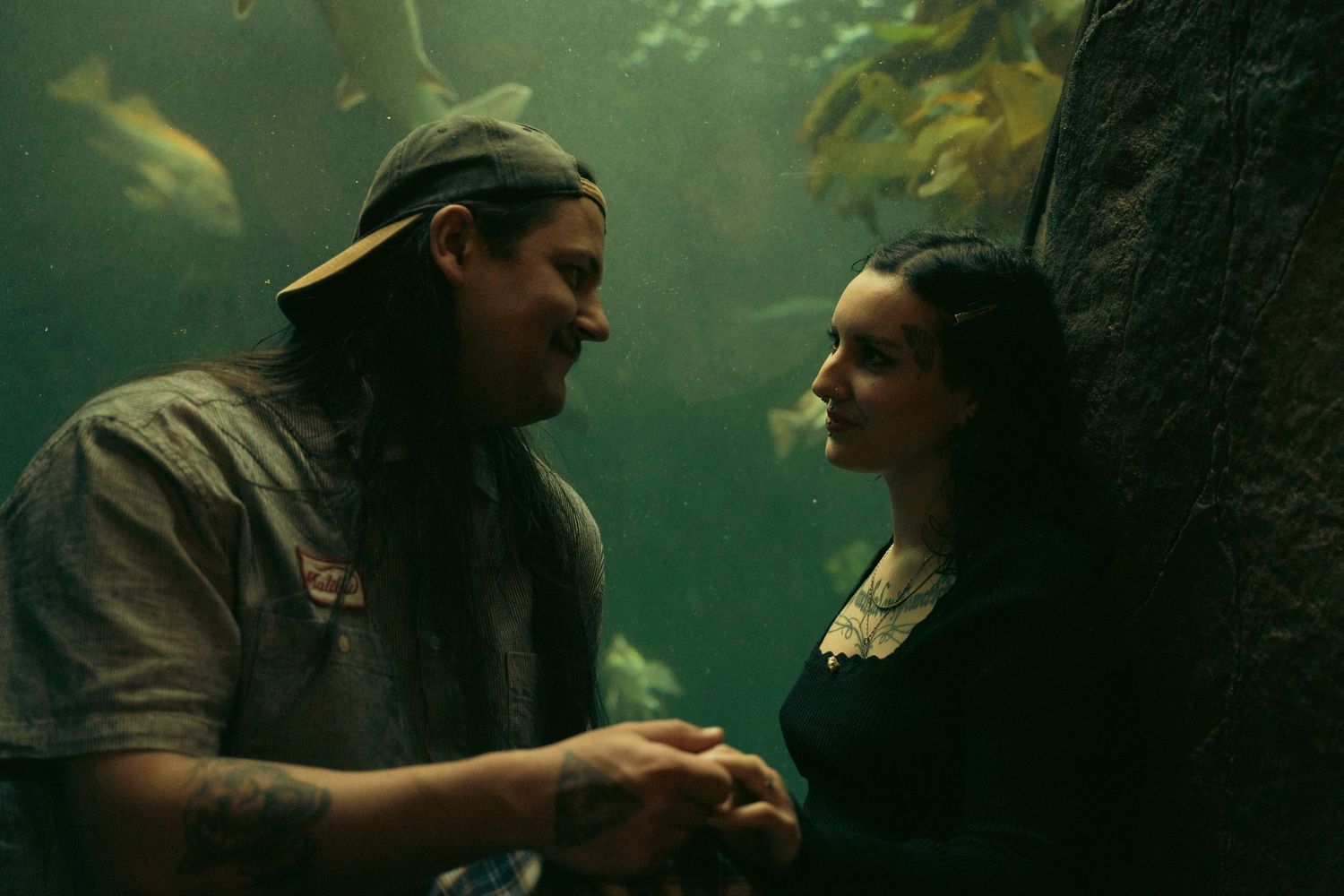 Couple sharing a romantic moment at an aquarium, surrounded by green underwater light and fish.