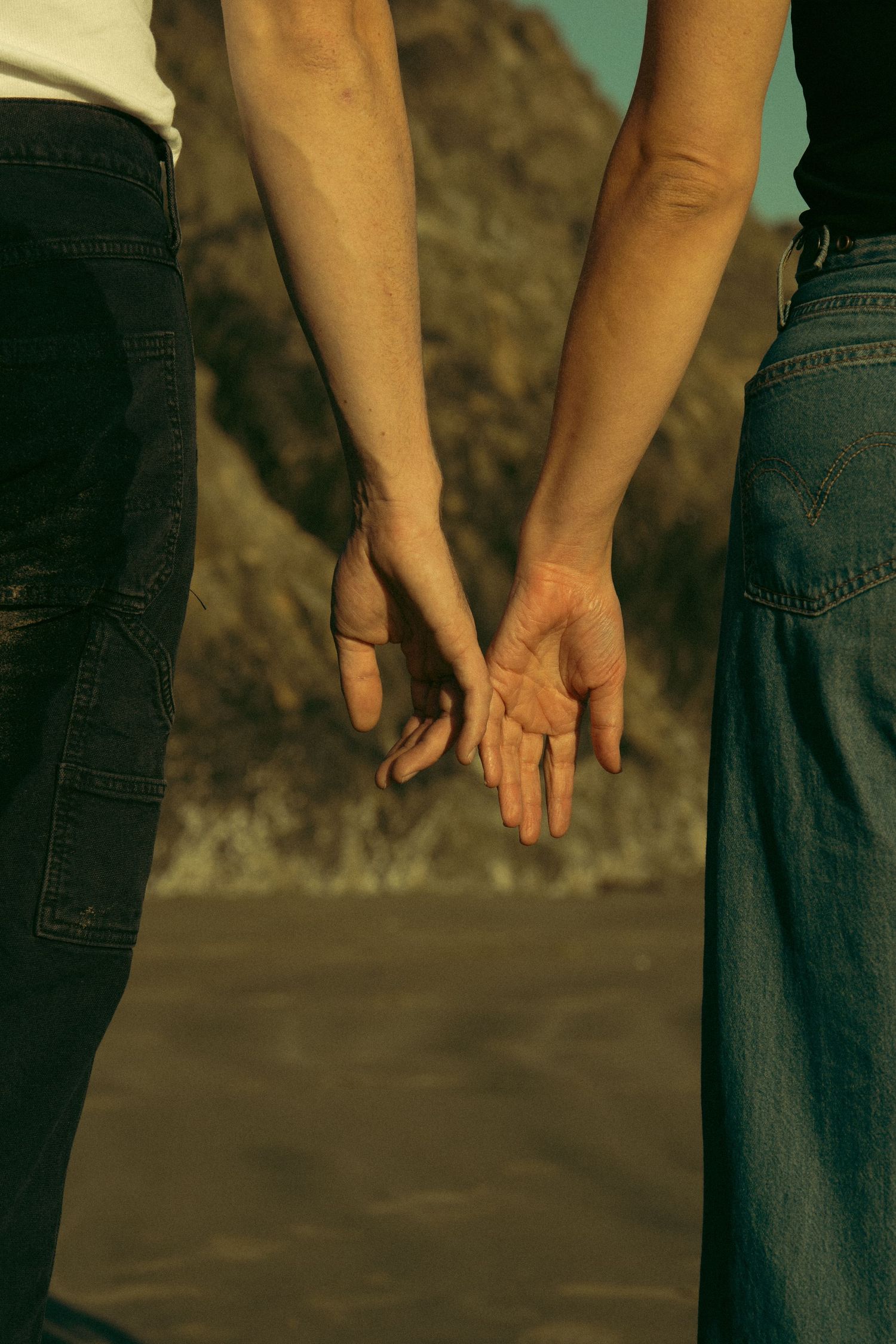 Close-up of two hands reaching toward each other against sunset backdrop.