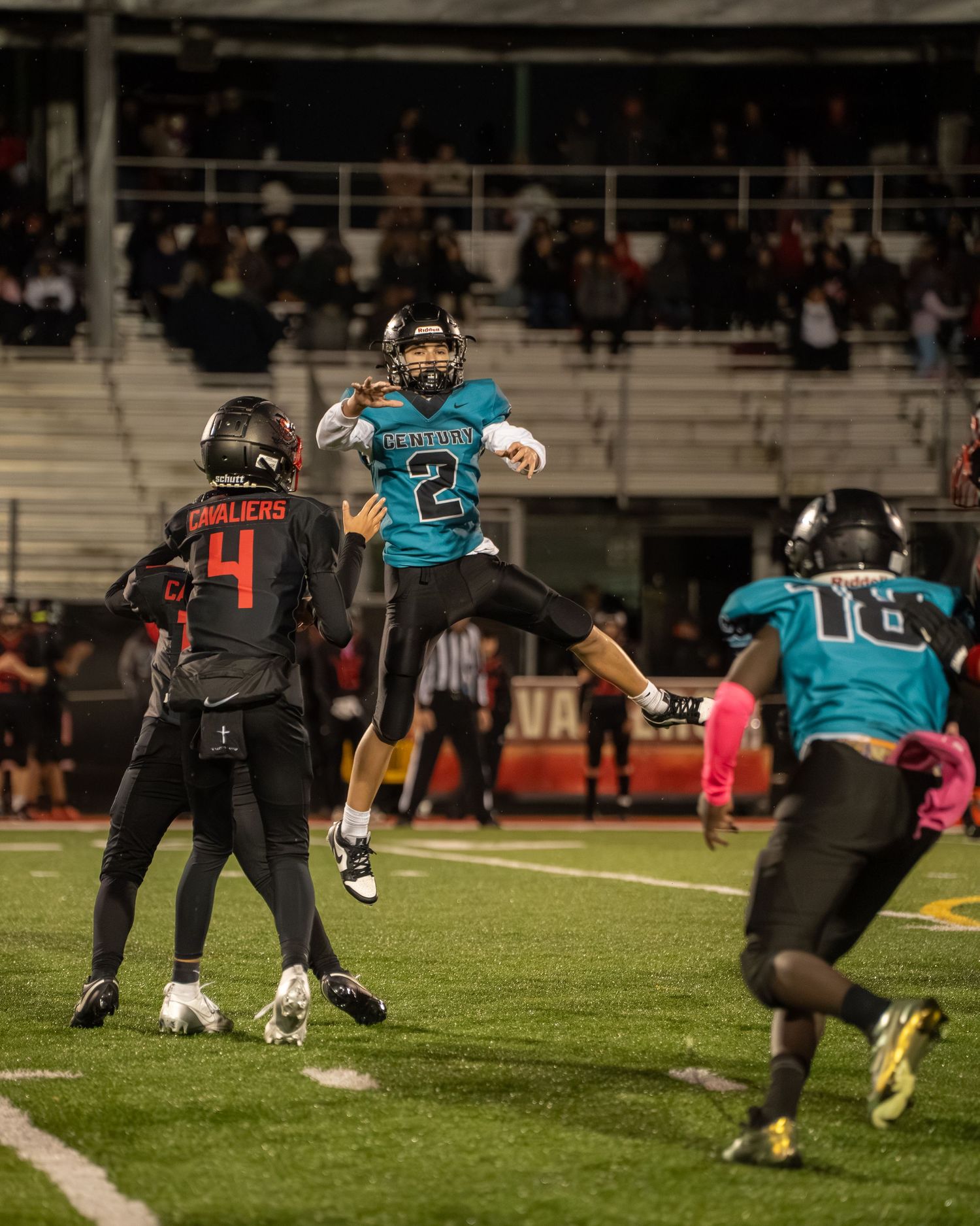 Multiple football players in teal and black uniforms line up in formation on field.