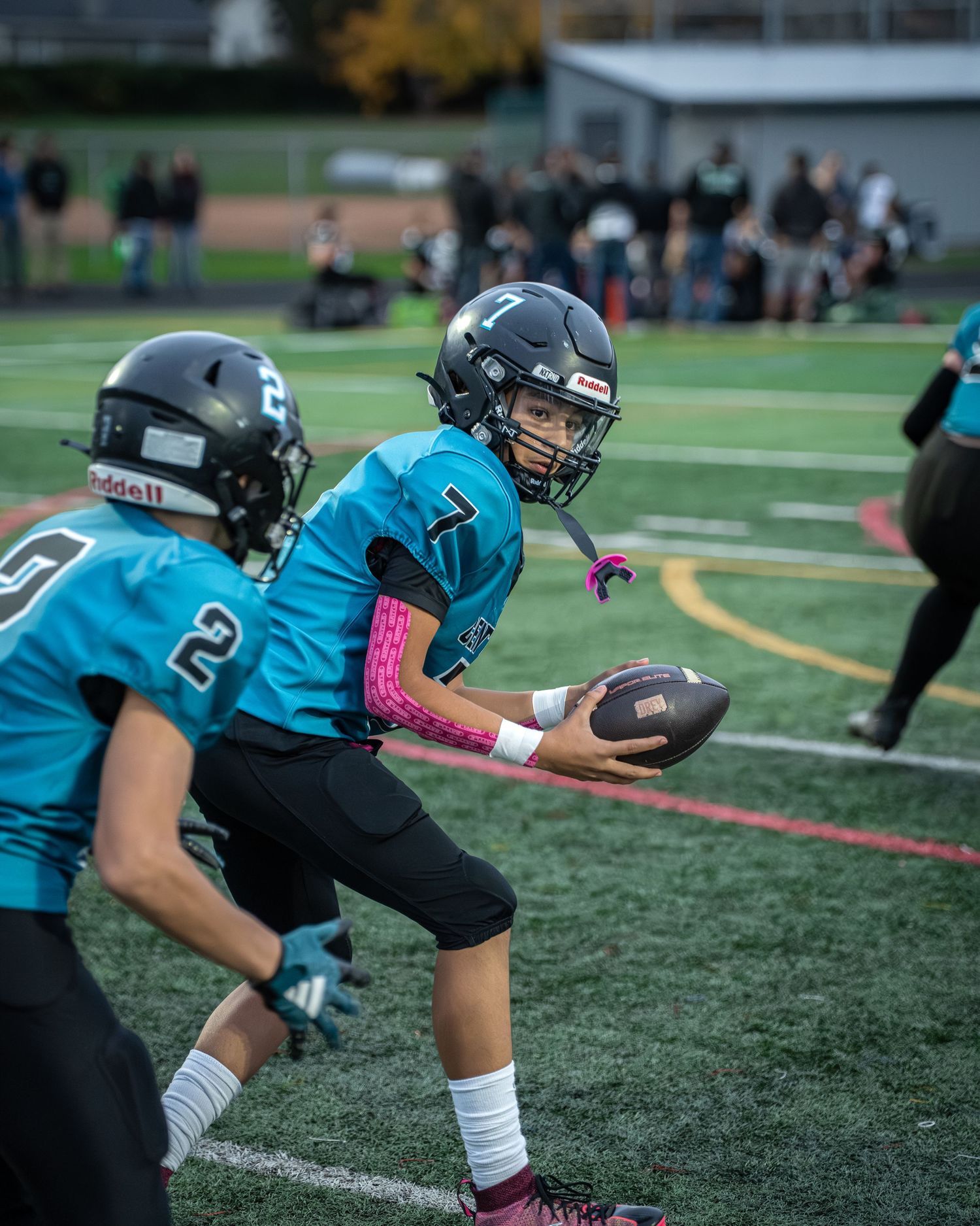 Football player in teal jersey prepares to hand off ball during game play.