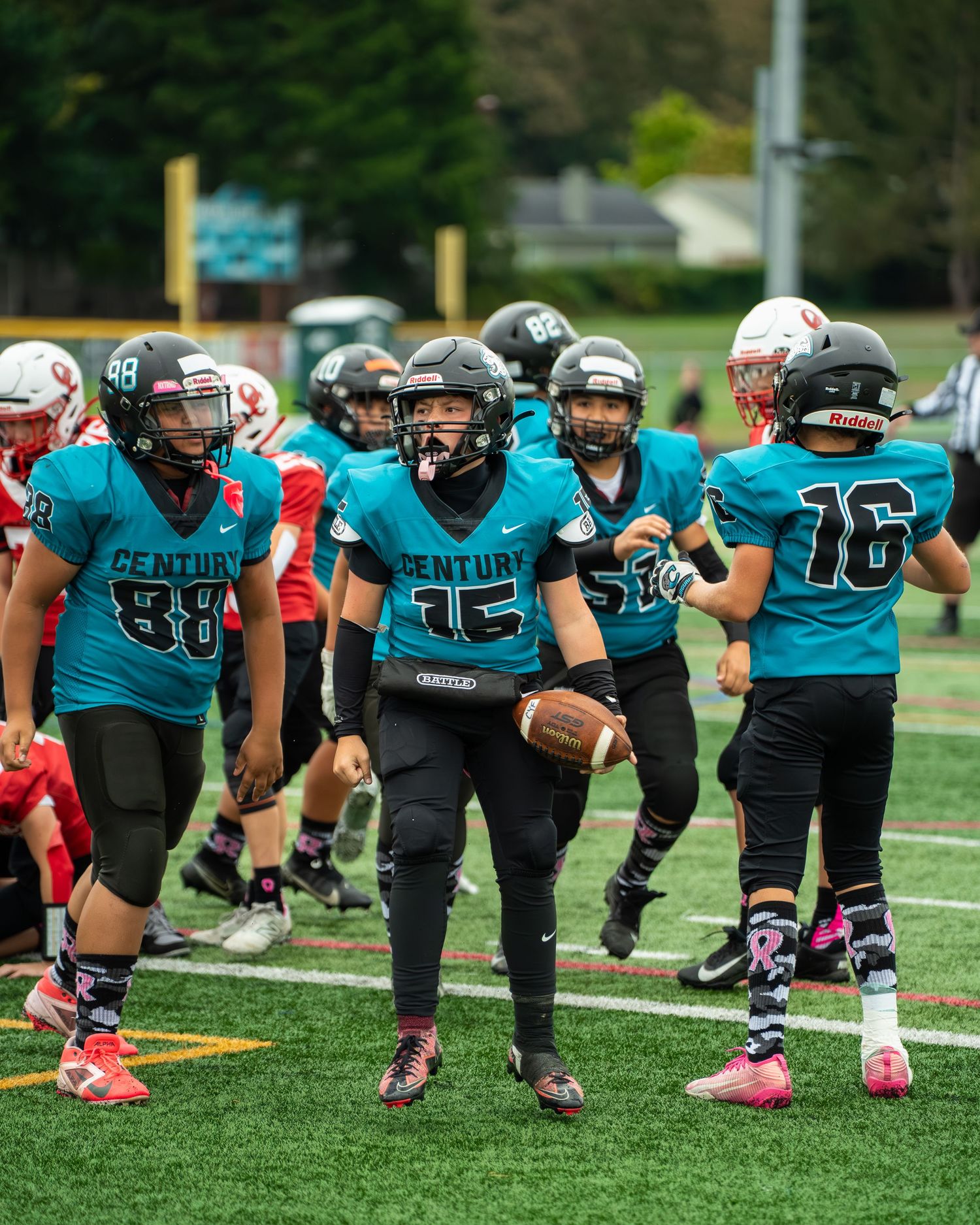 Football team lined up in teal jerseys preparing for snap on grass field.