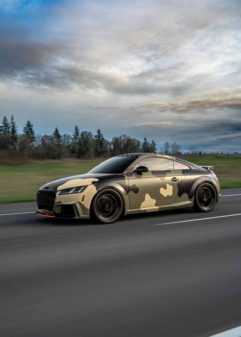 Performance cars with desert camouflage wraps racing along a scenic highway.