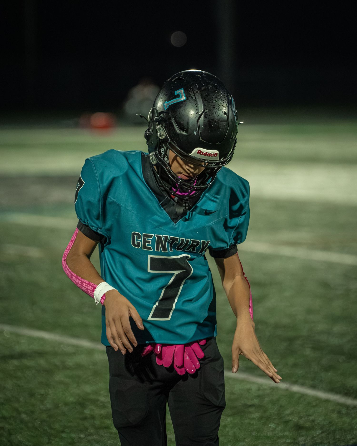 Player in teal jersey number 7 stands ready on the football field at night.