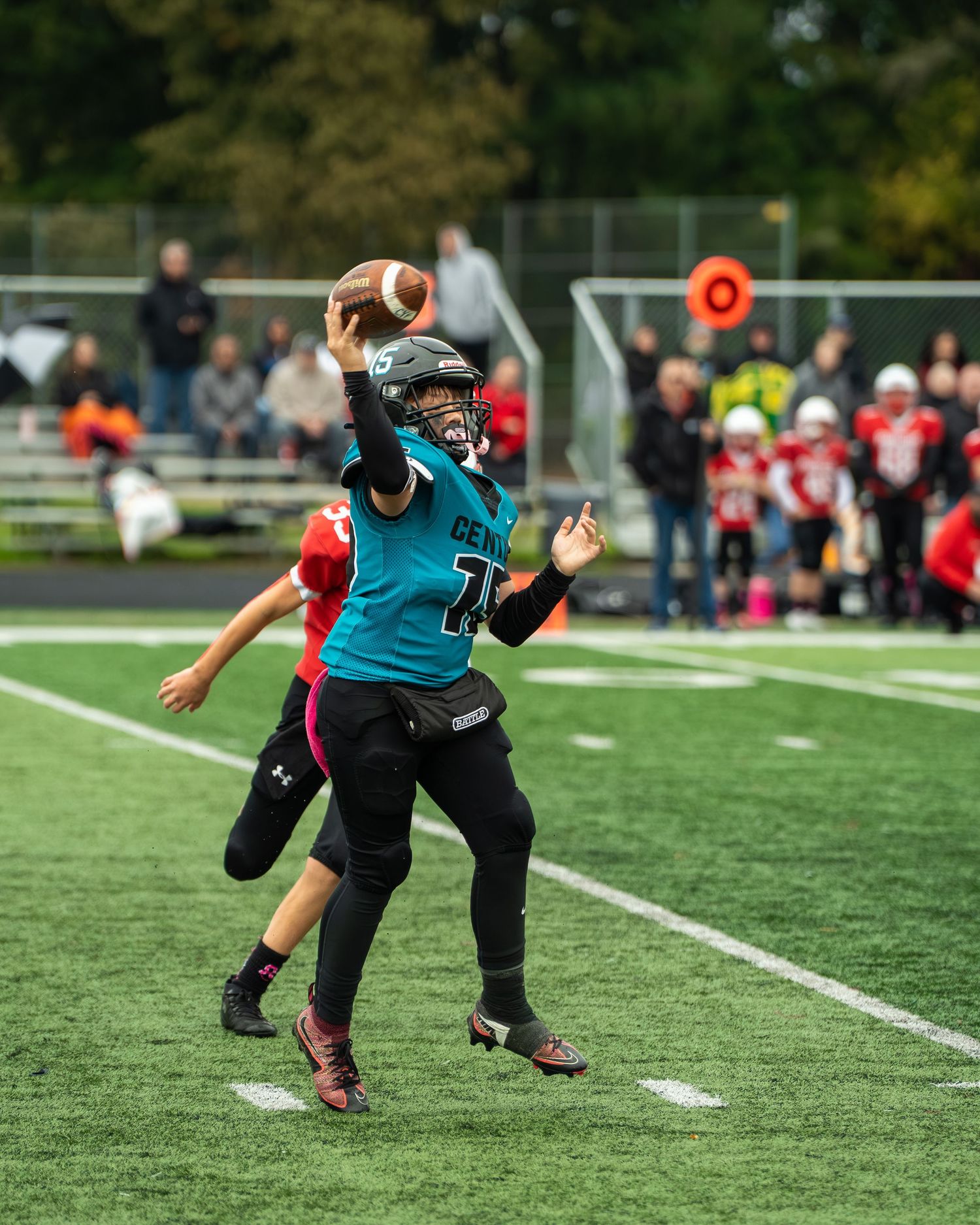 Football player in teal jersey dives to make a catch during gameplay on artificial turf.