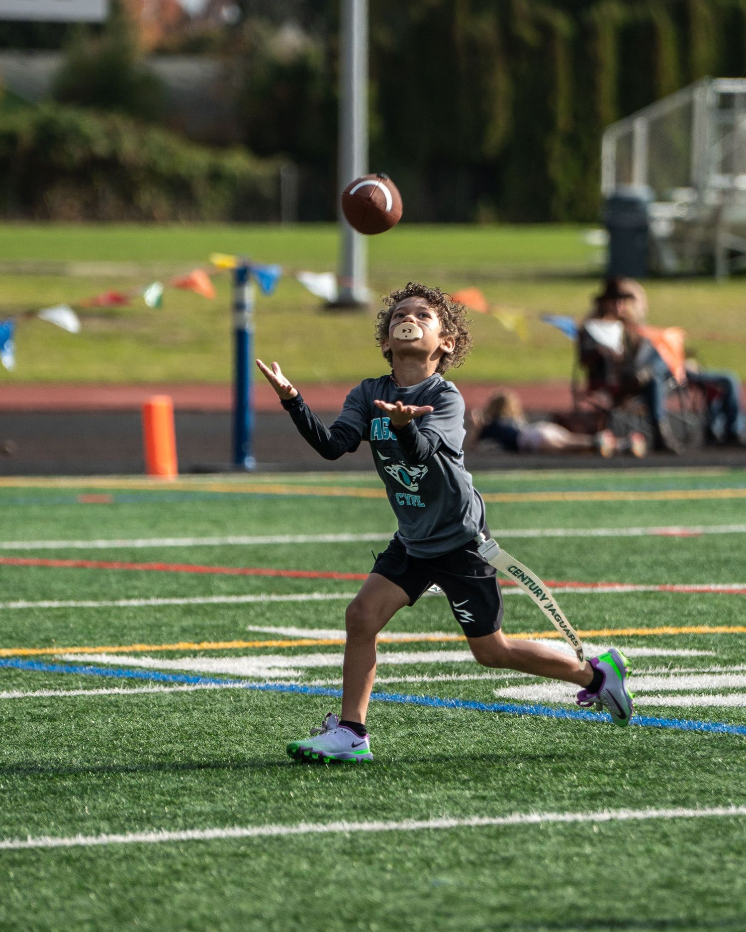 Football player in teal jersey diving to catch ball on artificial turf field.