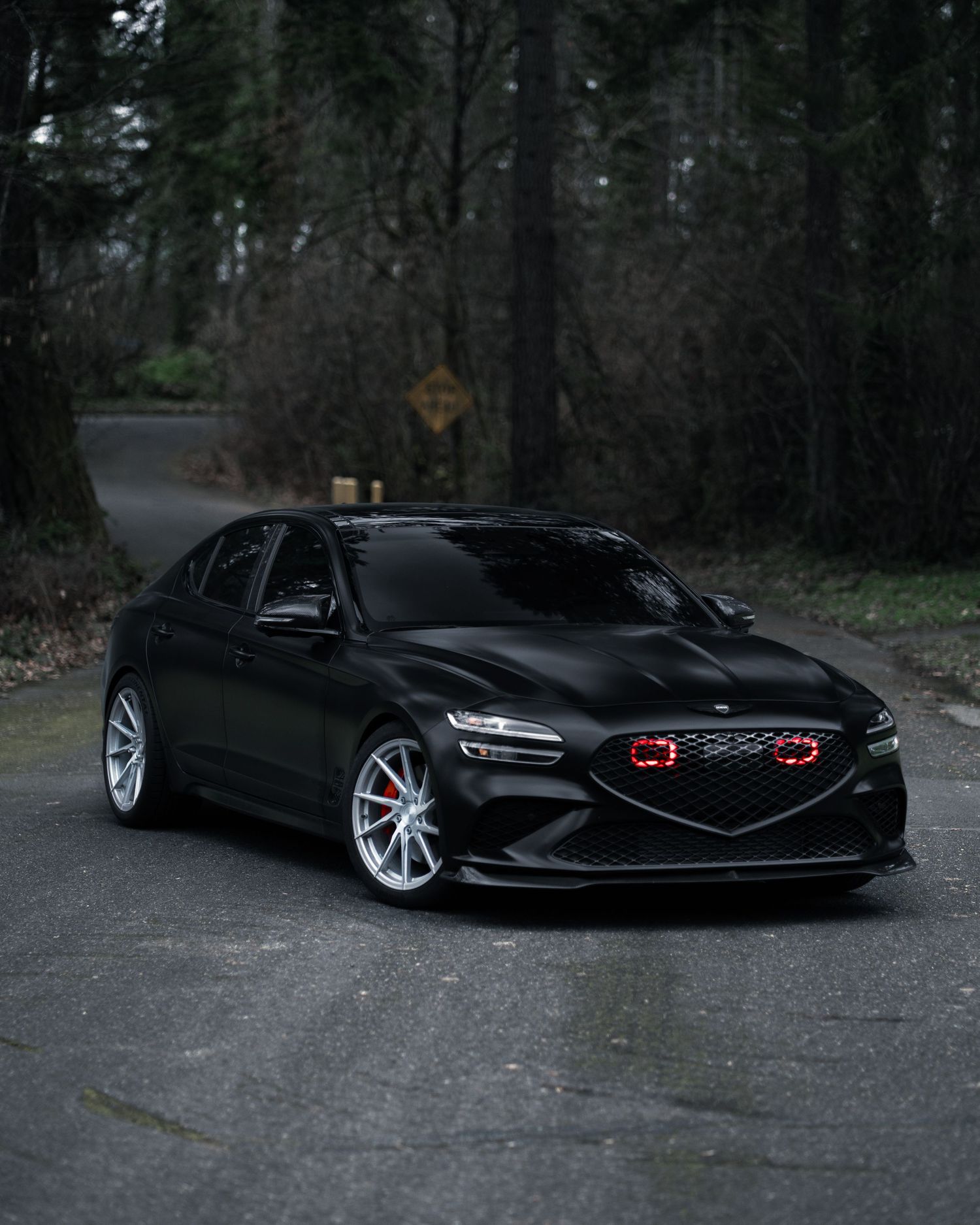 Black Genesis luxury sedan with glowing red headlights photographed in low light conditions.