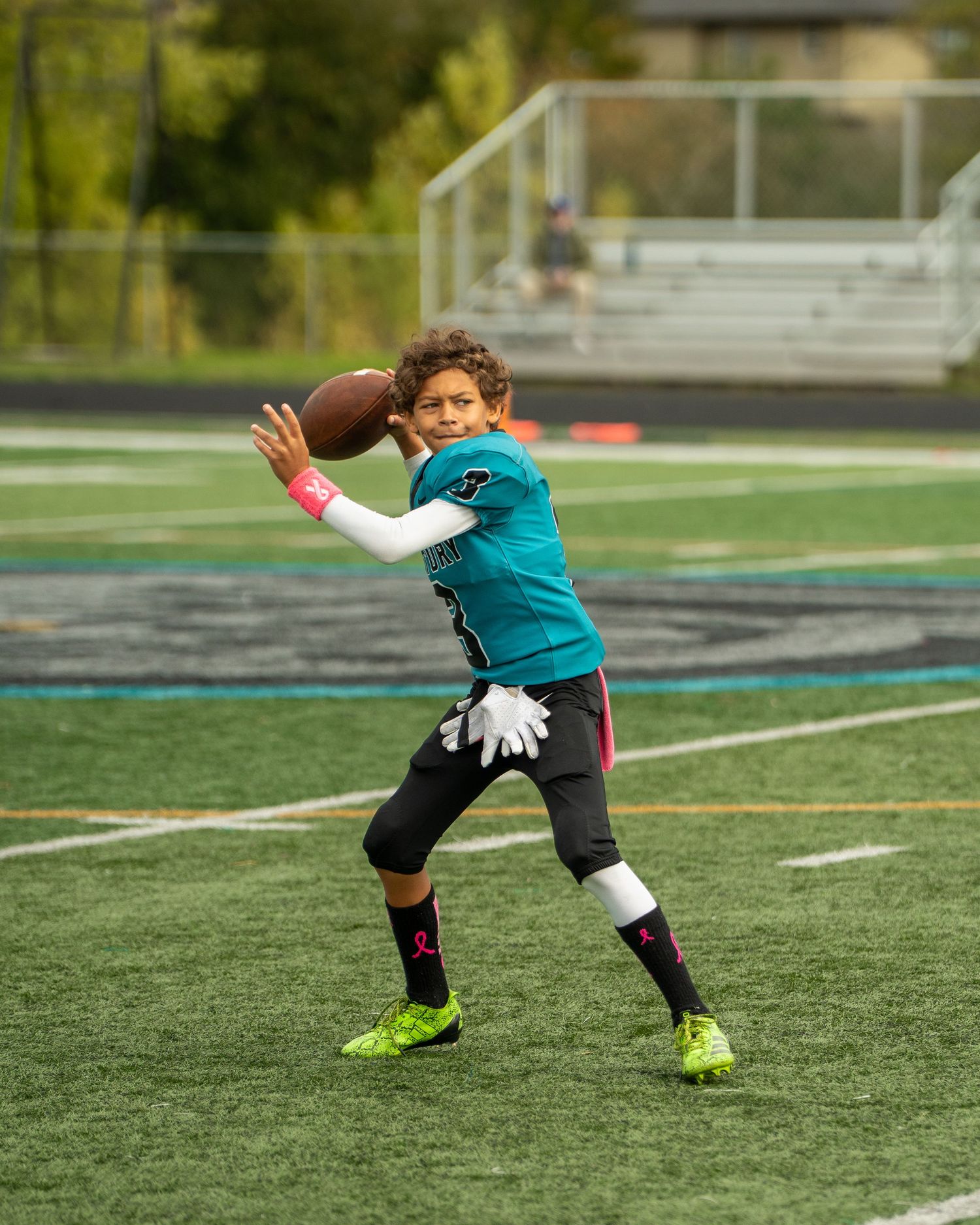 Youth football player in teal jersey practices catching stance with football.