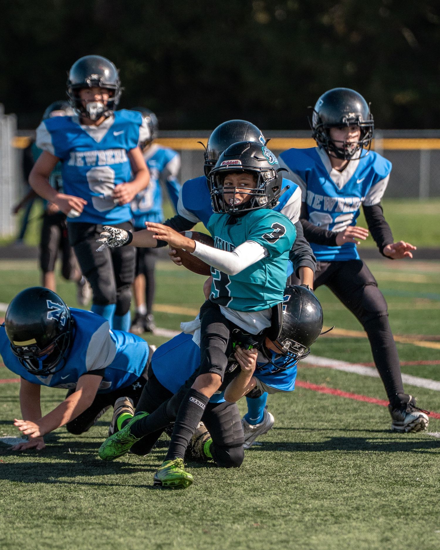 Football players in teal and blue uniforms execute diving drills during practice session.
