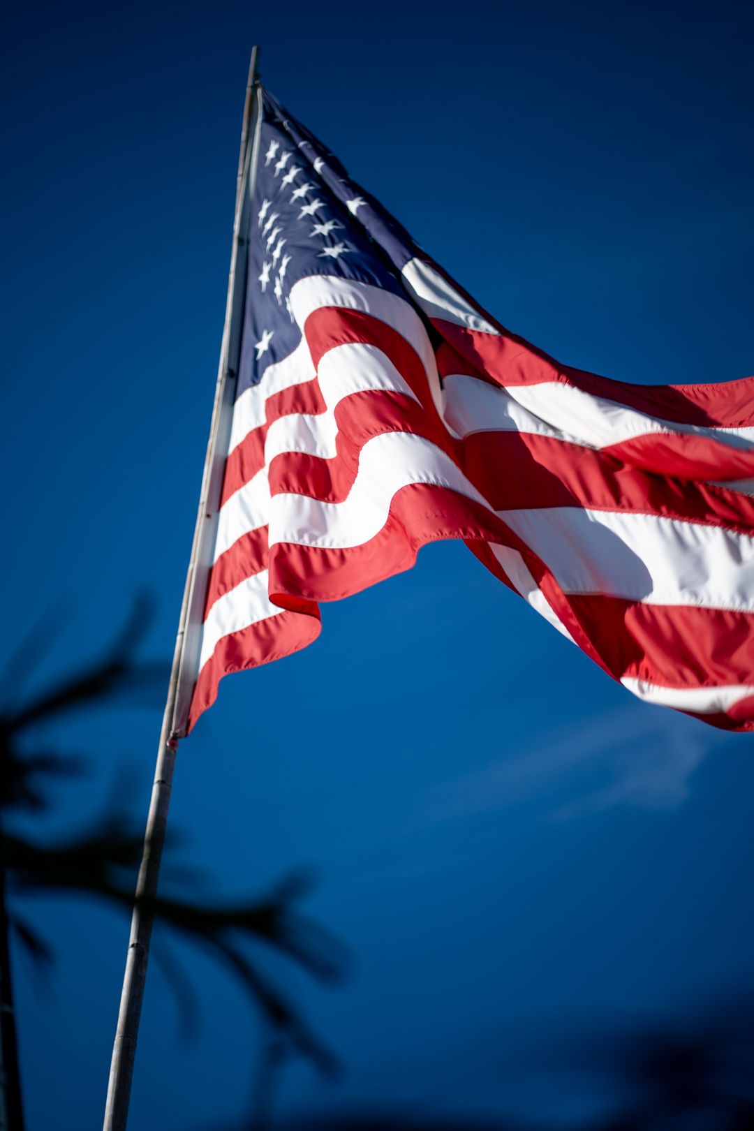 American flag waves against deep blue sky with dramatic lighting and contrast.