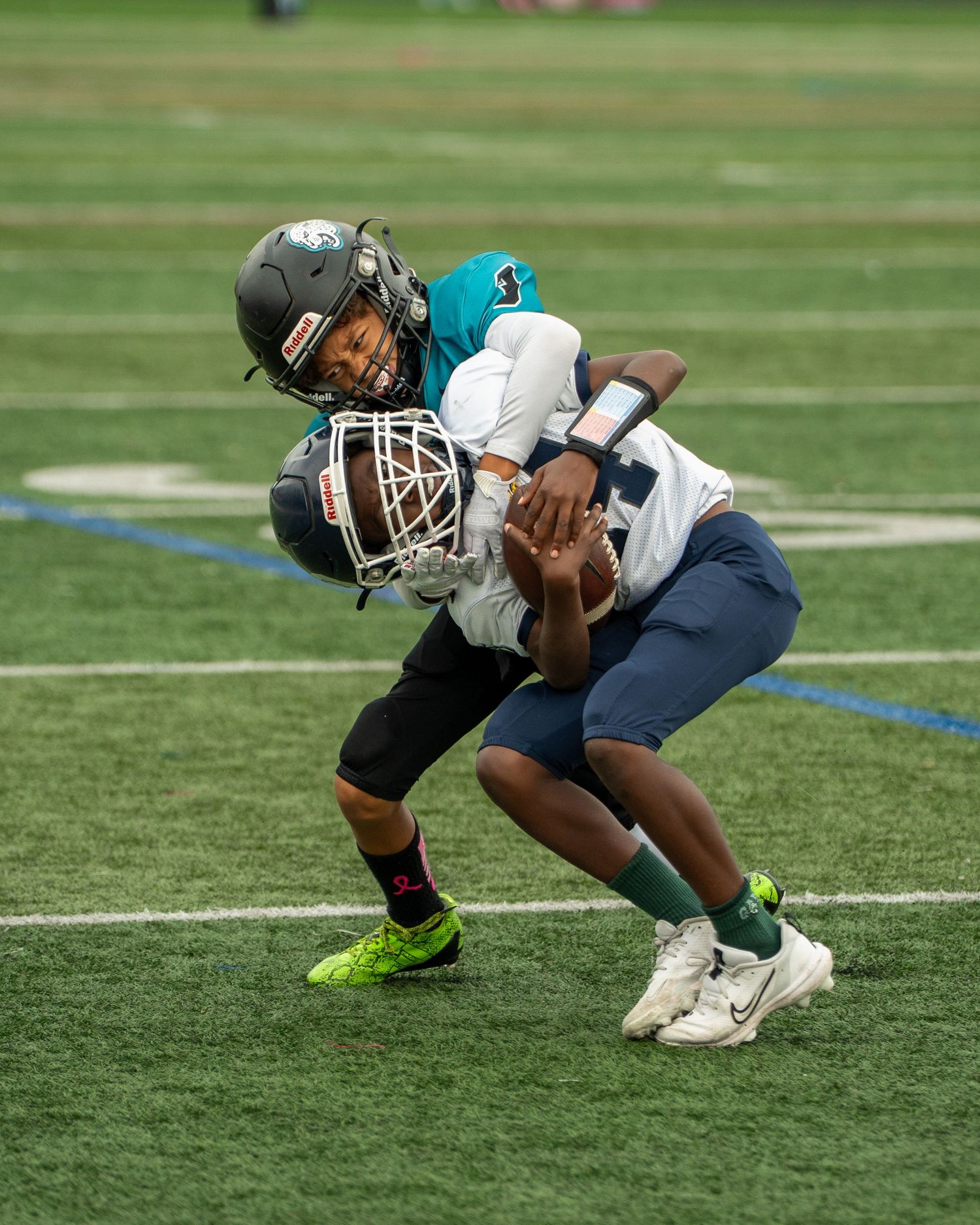 Young football players in teal jerseys practice defensive stances on a turf field.